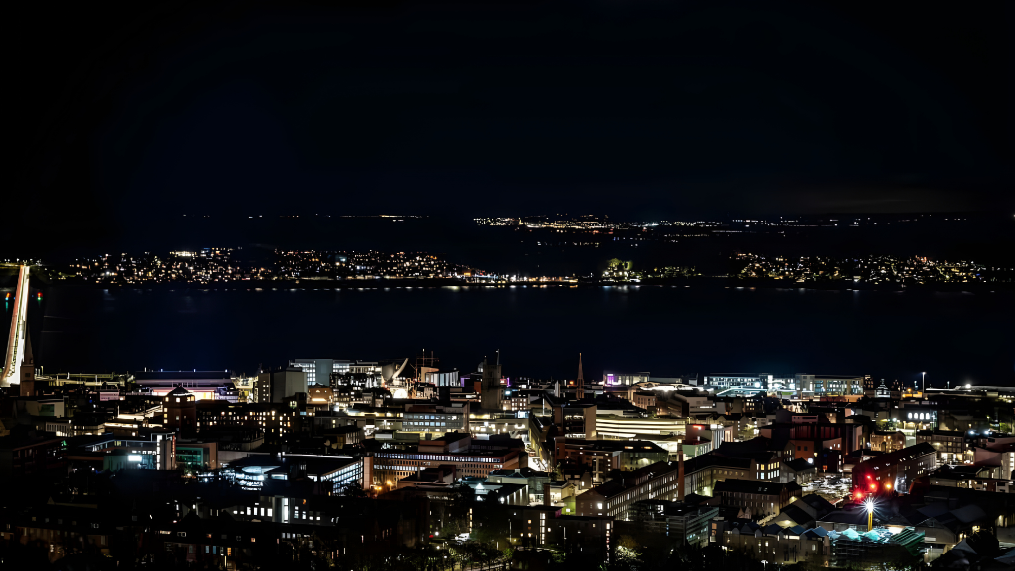 Dundee skyline at night with illuminated buildings along the water and distant hills, photographed by Kaelyn Robertson Sakura Property Collective, estate agents in Dundee & St Andrews.
