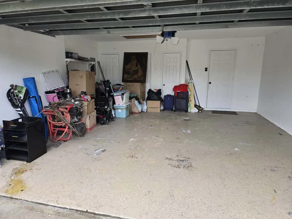 Empty garage with storage boxes, tools, and miscellaneous household items against the wall.