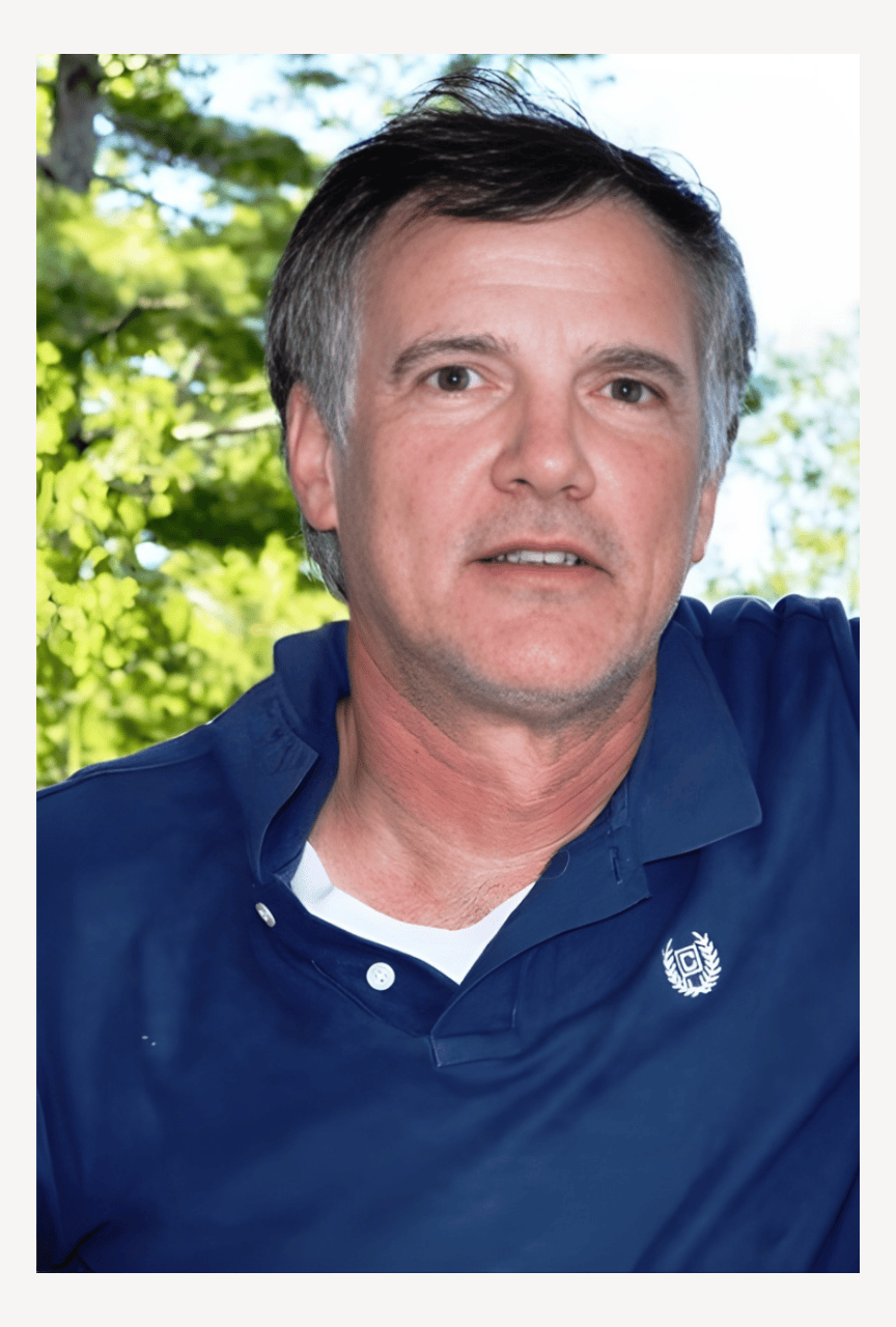 Author Peter Sarno with dark hair and light skin is outdoors, with green trees in the background. He is wearing a blue collared shirt and looks directly at the camera.