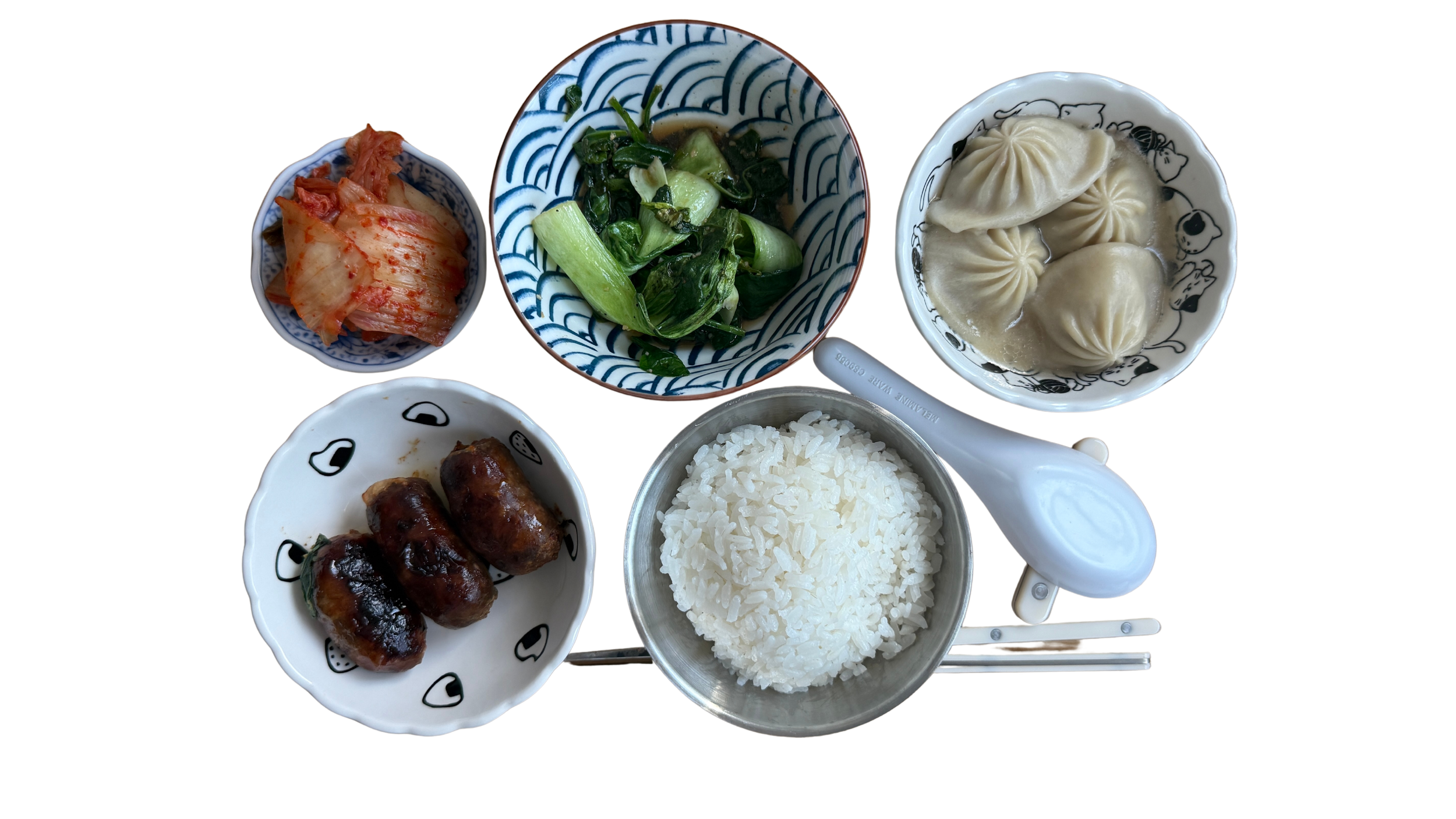 A traditional Asian meal with white rice, steamed soup dumplings, sausages, pickled vegetables, stir-fried green vegetables, and kimchi served in small bowls with chopsticks and a rice paddle.