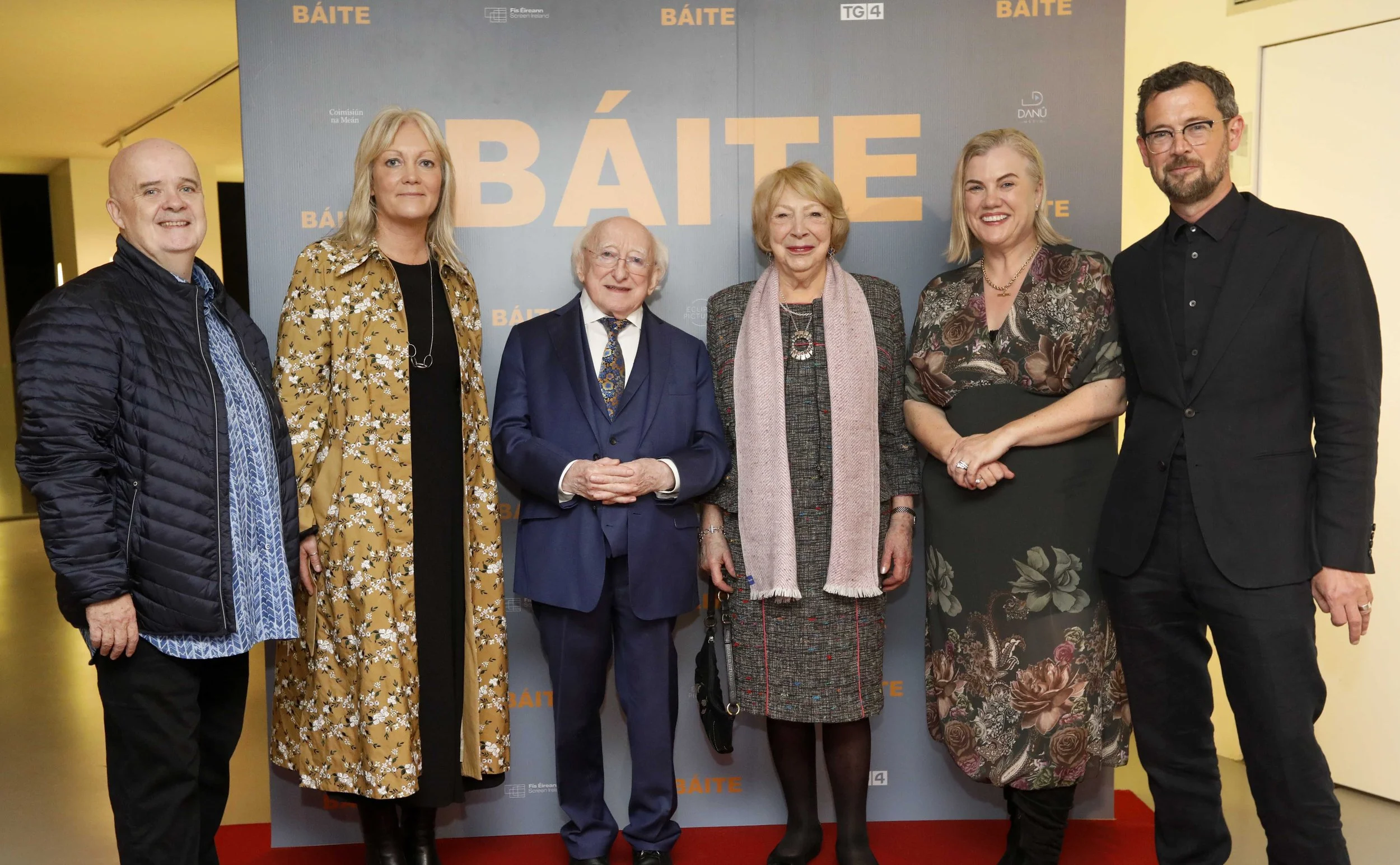 Seven people standing in front of a blue and yellow backdrop, smiling for the camera at a formal event.