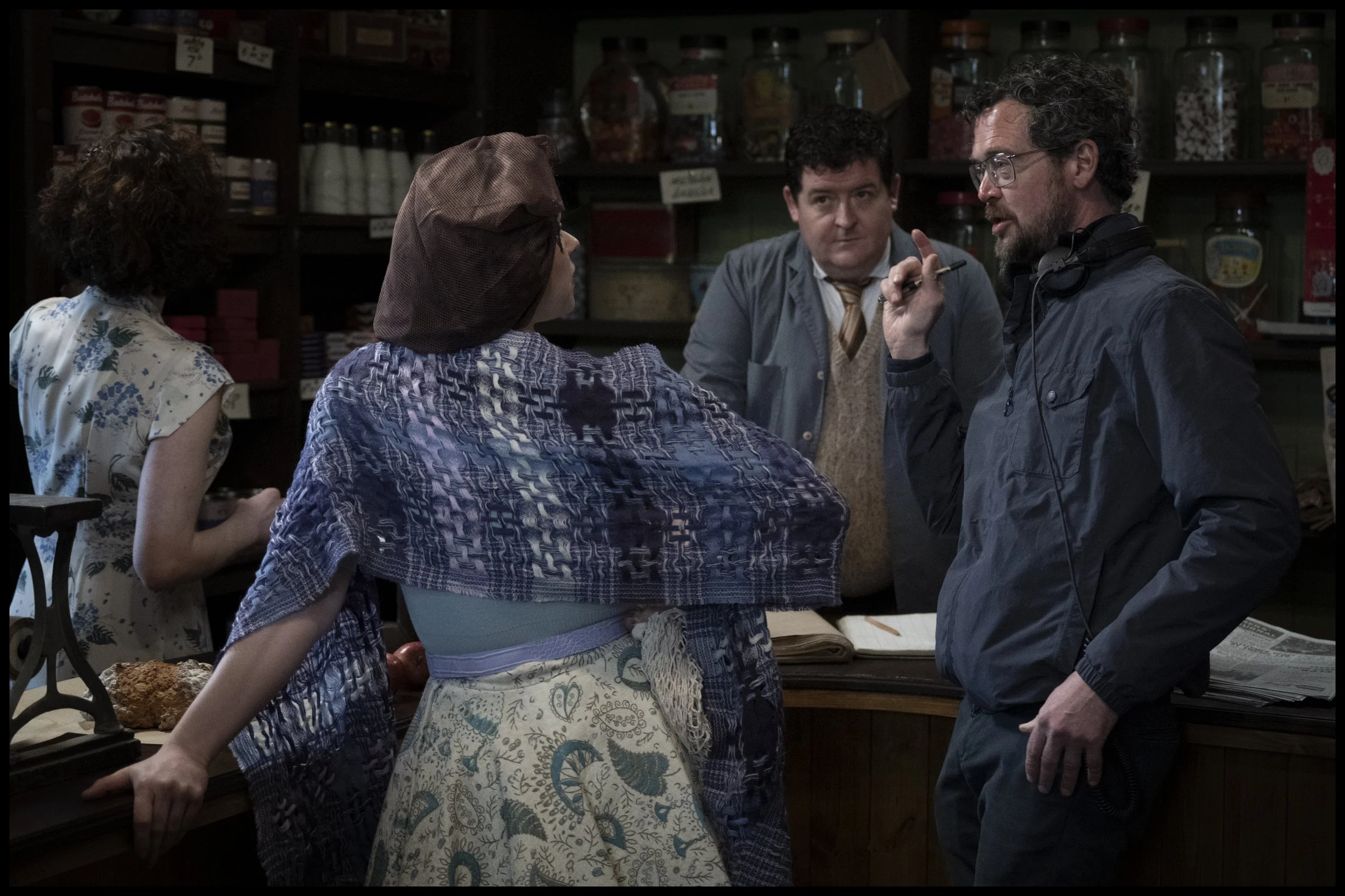 Four people standing and talking inside a store, shelves with various goods in the background.