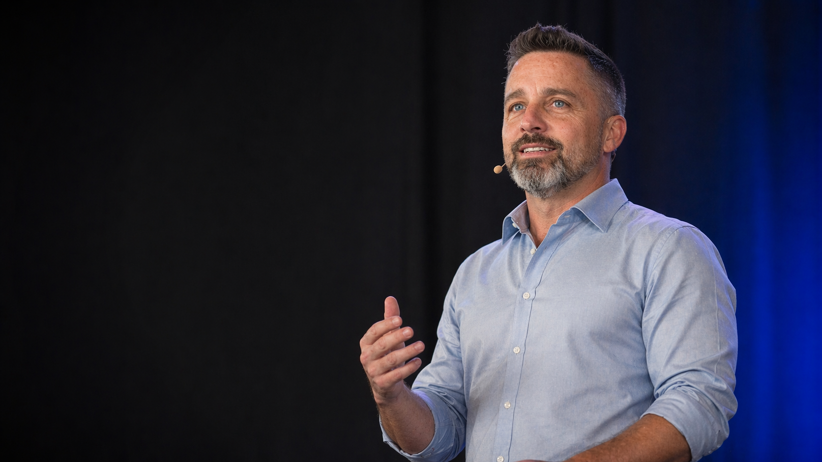 Craig Sawyer speaking on stage with a headset microphone against a dark blue background.