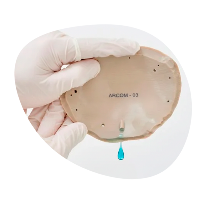 Persona con guantes sostiene un dispositivo médico en forma de corazón, con una gota azul que cae del centro.