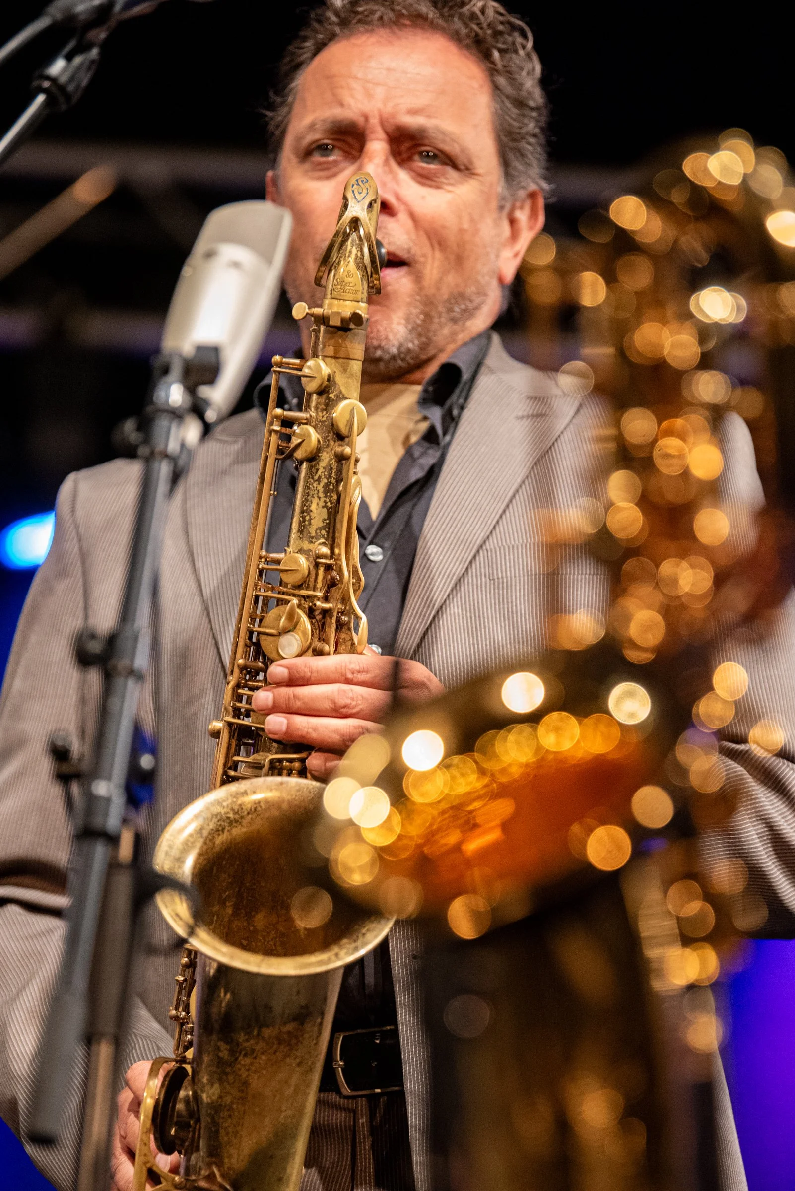 Ein Mann spielt Saxophon auf einer Bühne, im Hintergrund sind Lichter und eine Weihnachtsdekoration zu sehen.