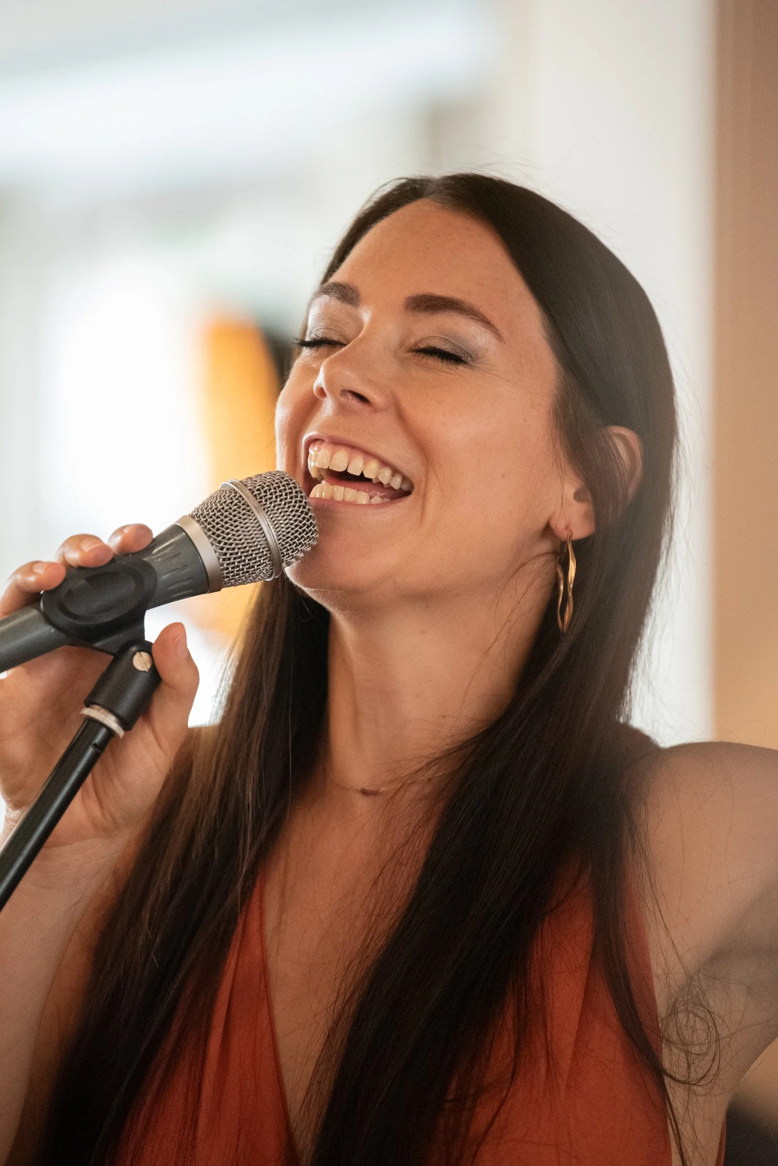 Junge Frau singt mit geschlossnen Augen in ein Mikrofon, lächelnd.