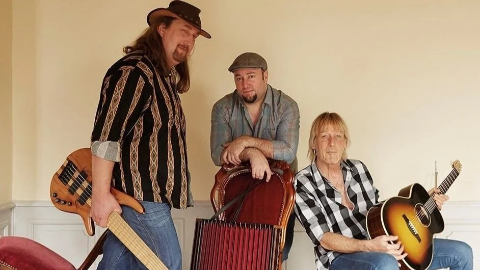 Drei Männer mit Musikinstrumenten, in einem Raum mit hellgelber Wand.