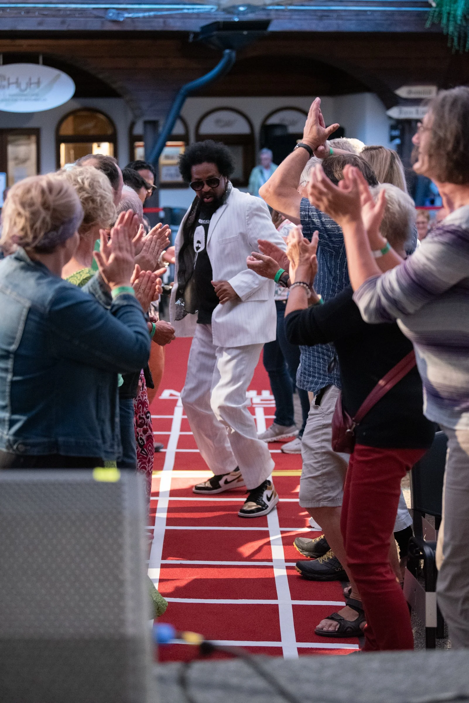 Mensch tanzt auf einer Tanzfläche mit einer Gruppe von Menschen, umgeben von Zuschauern, bei einer Veranstaltung in einem Veranstaltungsraum.