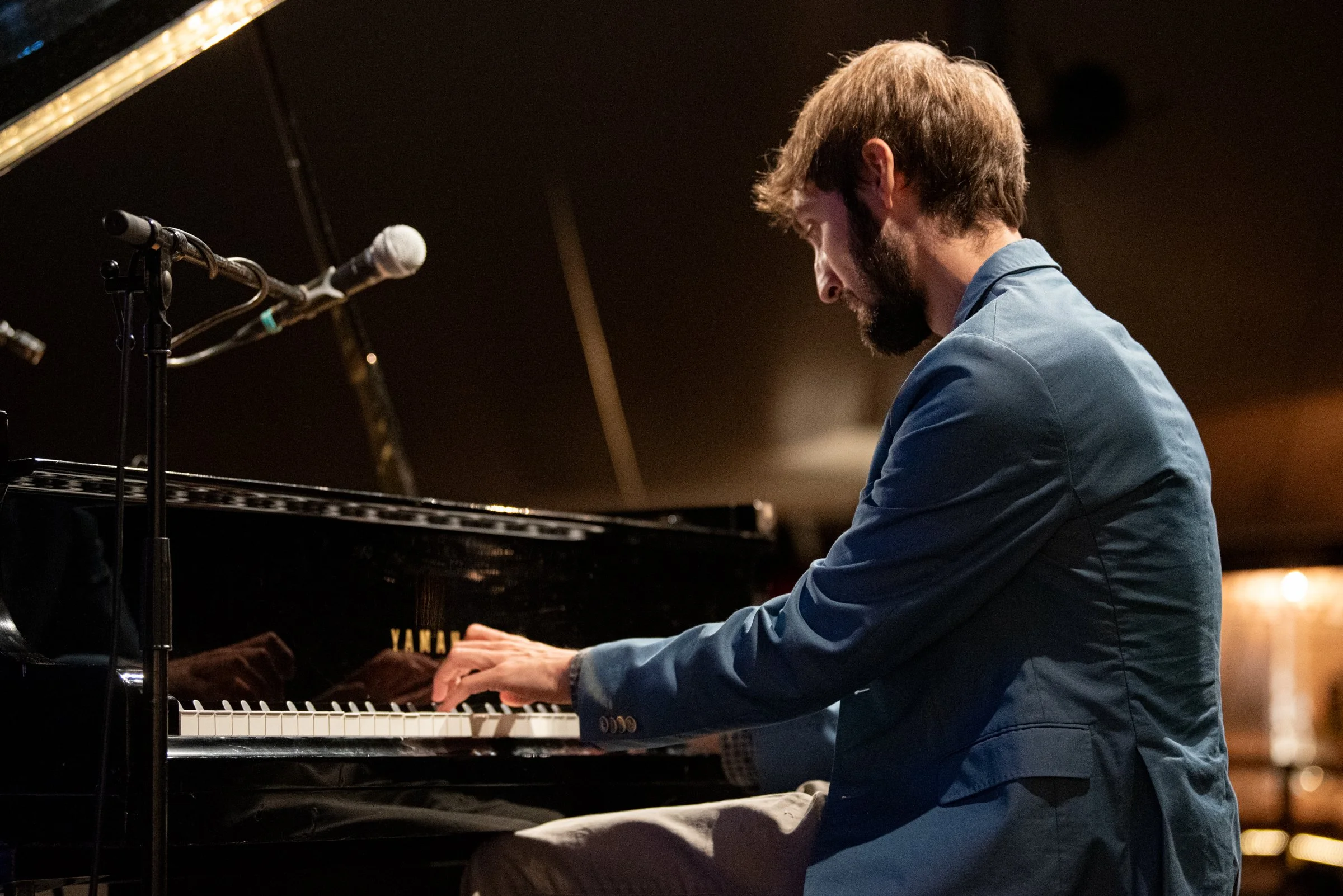 Mann spielt Klavier in einem dunklen Raum, Mikrofon neben ihm.