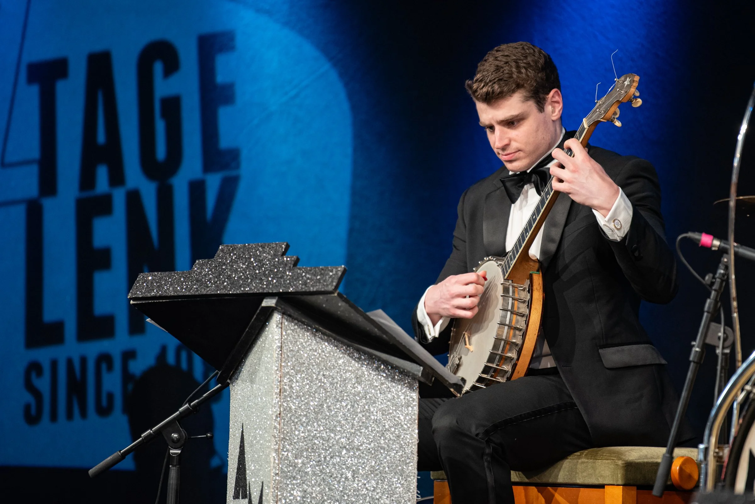 Junger Mann in Smoking spielt Banjo auf einer Bühne bei einem Musikfestival.