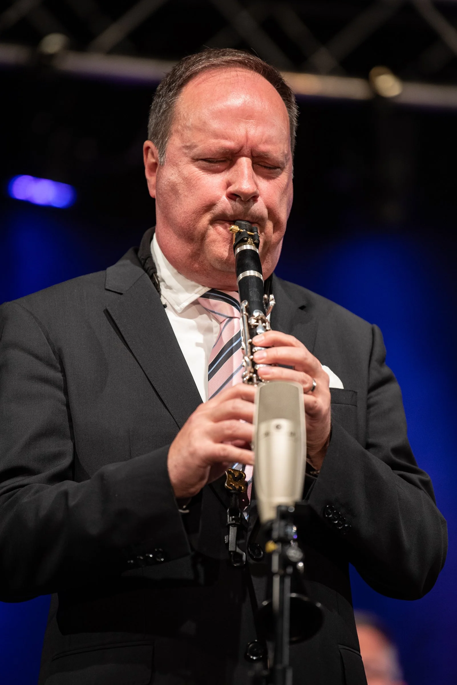 Ein Mann in Anzug spielt auf einer Bühne Saxophon, mit geschlossenem Gesicht und konzentrierter Mimik.