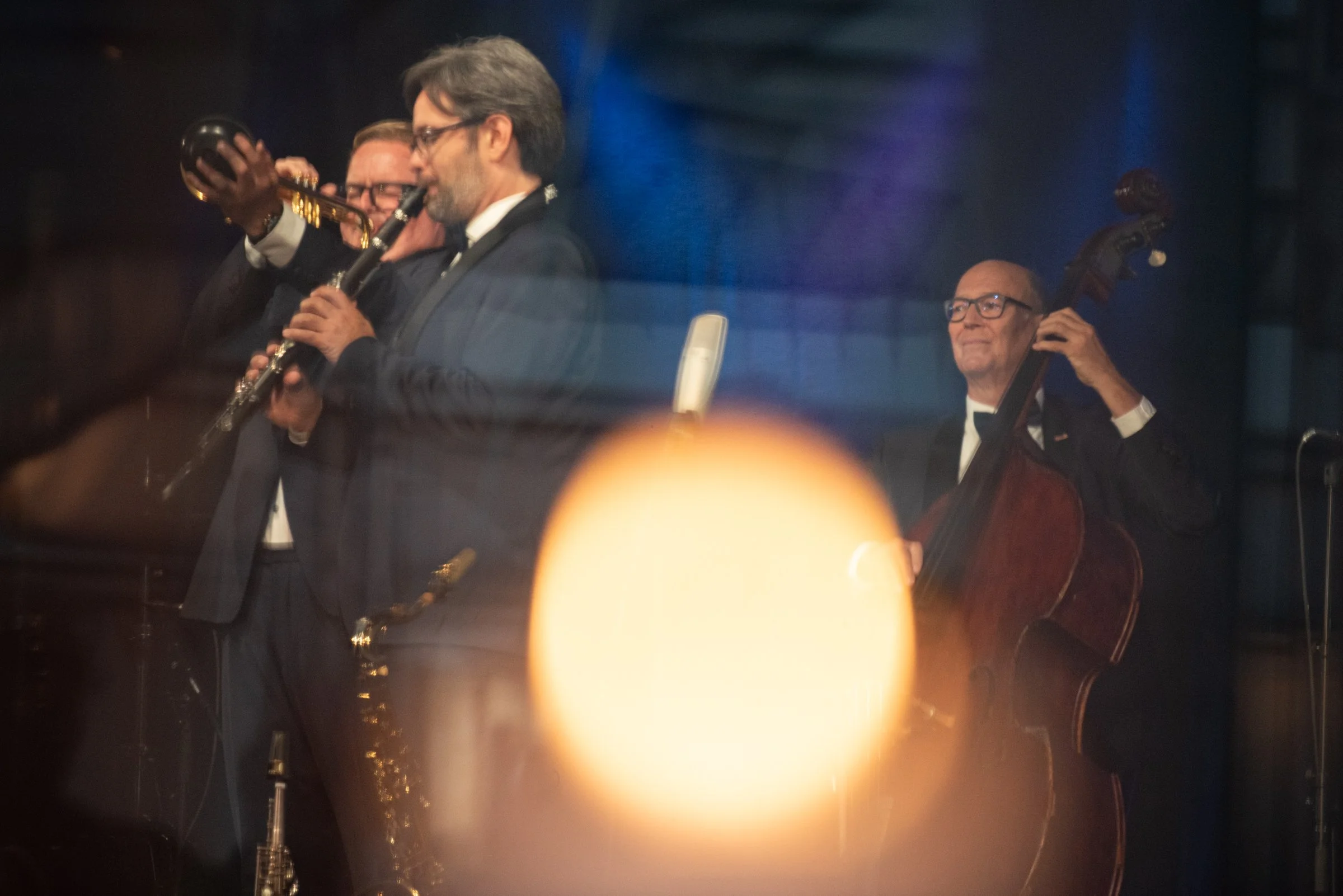 Vier Musiker in formeller Kleidung spielen auf einer Bühne, einer spielt Klarinette, einer flößt, einer auf einem Standbass, im Hintergrund blauer und violetter Bühnenlicht.