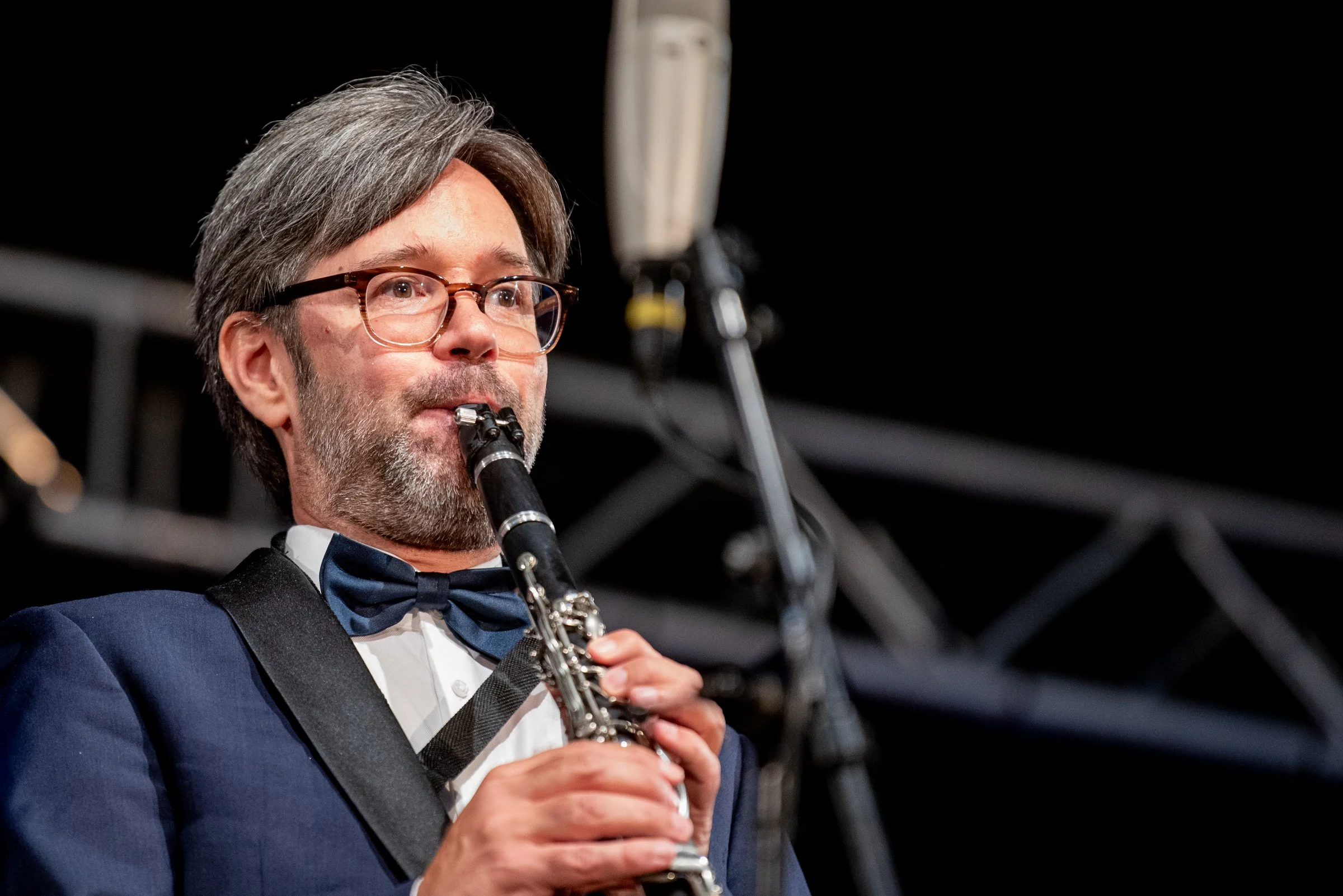 Mann in formeller Kleidung spielt auf der Klarinette bei einer Aufführung auf der Bühne.