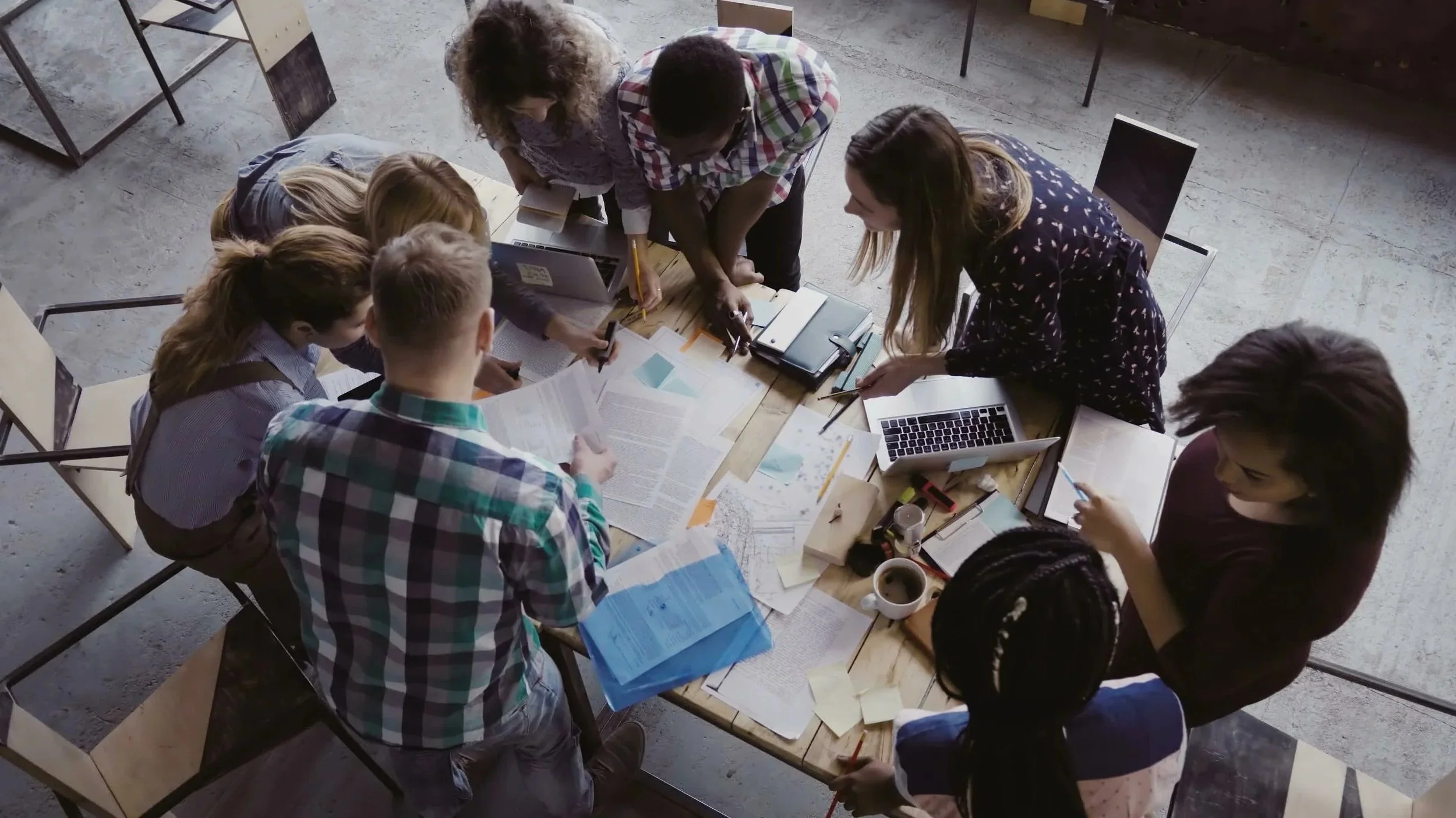 A group of people gathered around a table with papers, laptops, and stationery, engaged in a collaborative discussion or meeting.
