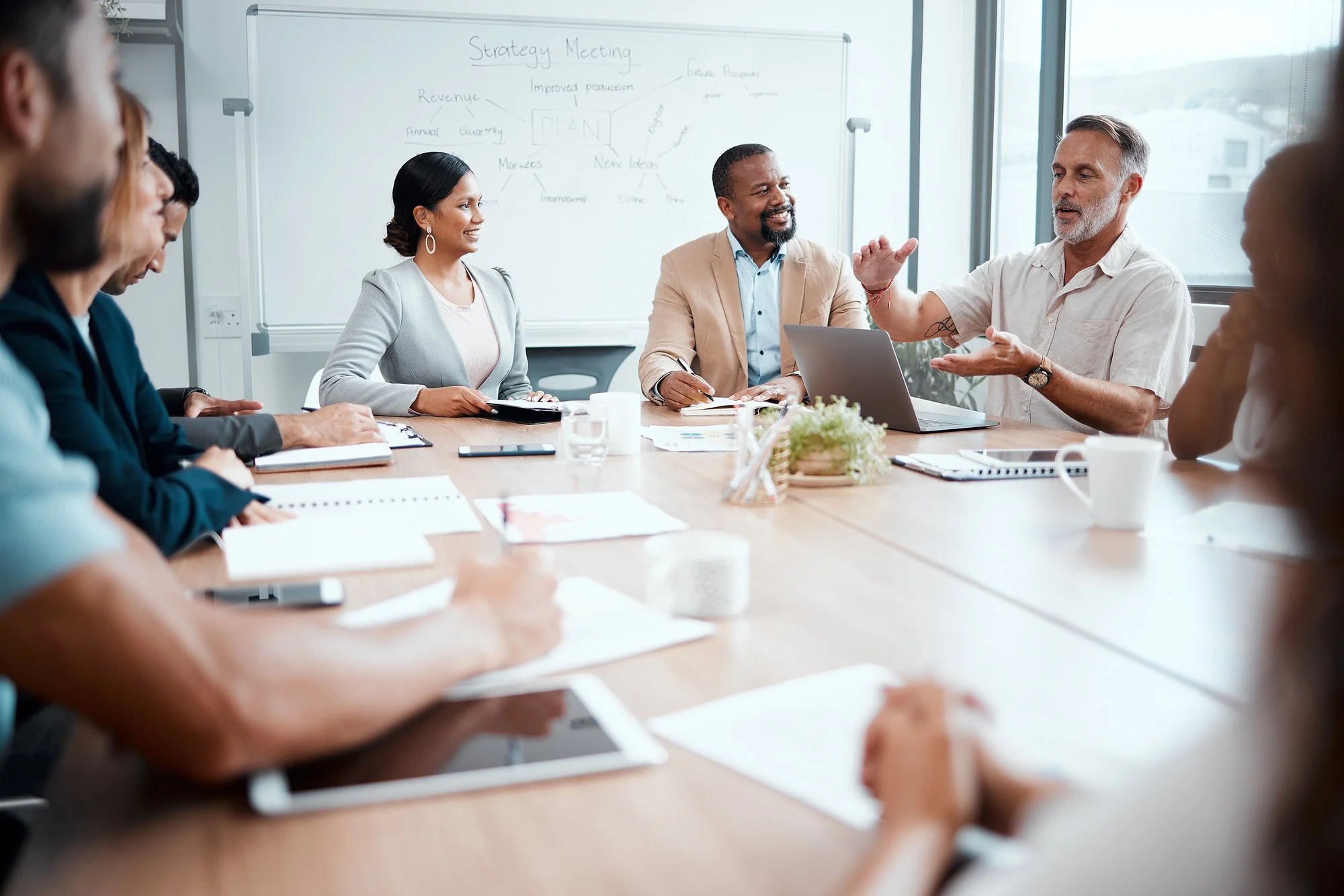 Business team in a strategy meeting around a conference table with a whiteboard behind them displaying a mind map related to planning and future prospects.