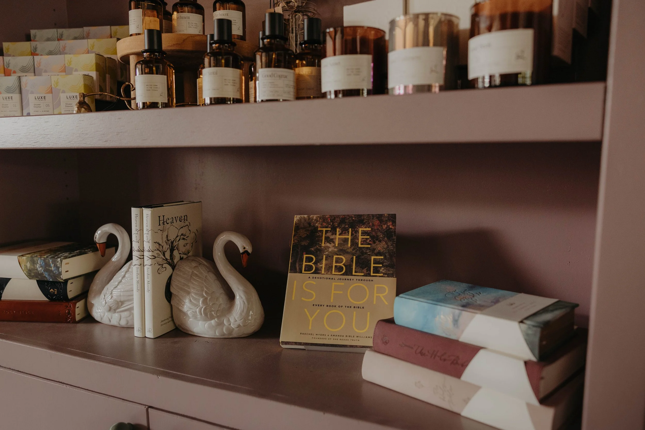 Books, candles, and decorative swan figurines on a shelf in a cozy, dimly-lit space.