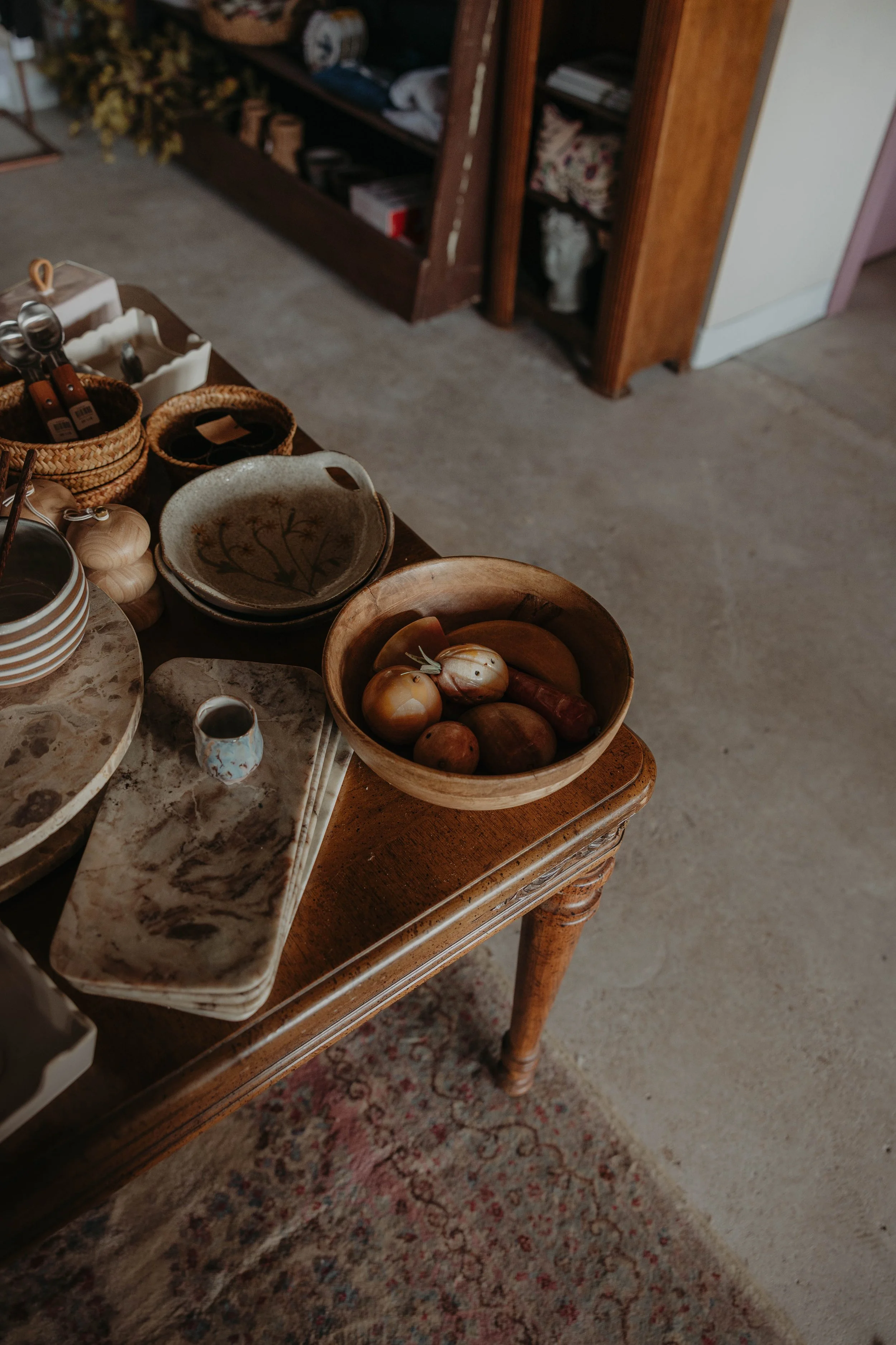 A wooden table displaying various ceramic bowls and plates filled with onions, garlic, and other kitchen items in a cozy interior setting.