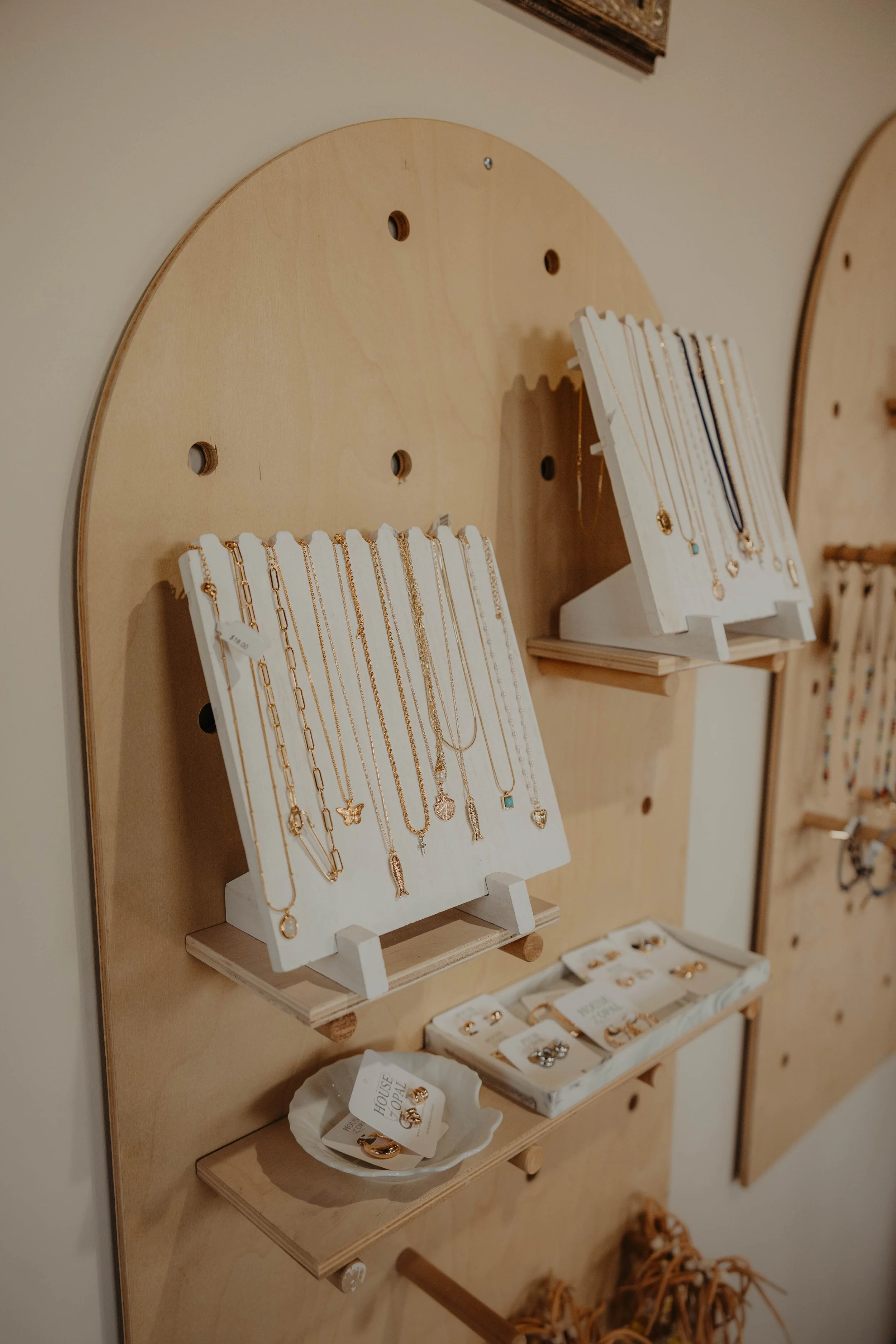 Display of jewelry, specifically necklaces and earrings, arranged on white and wooden stands in a retail setting.