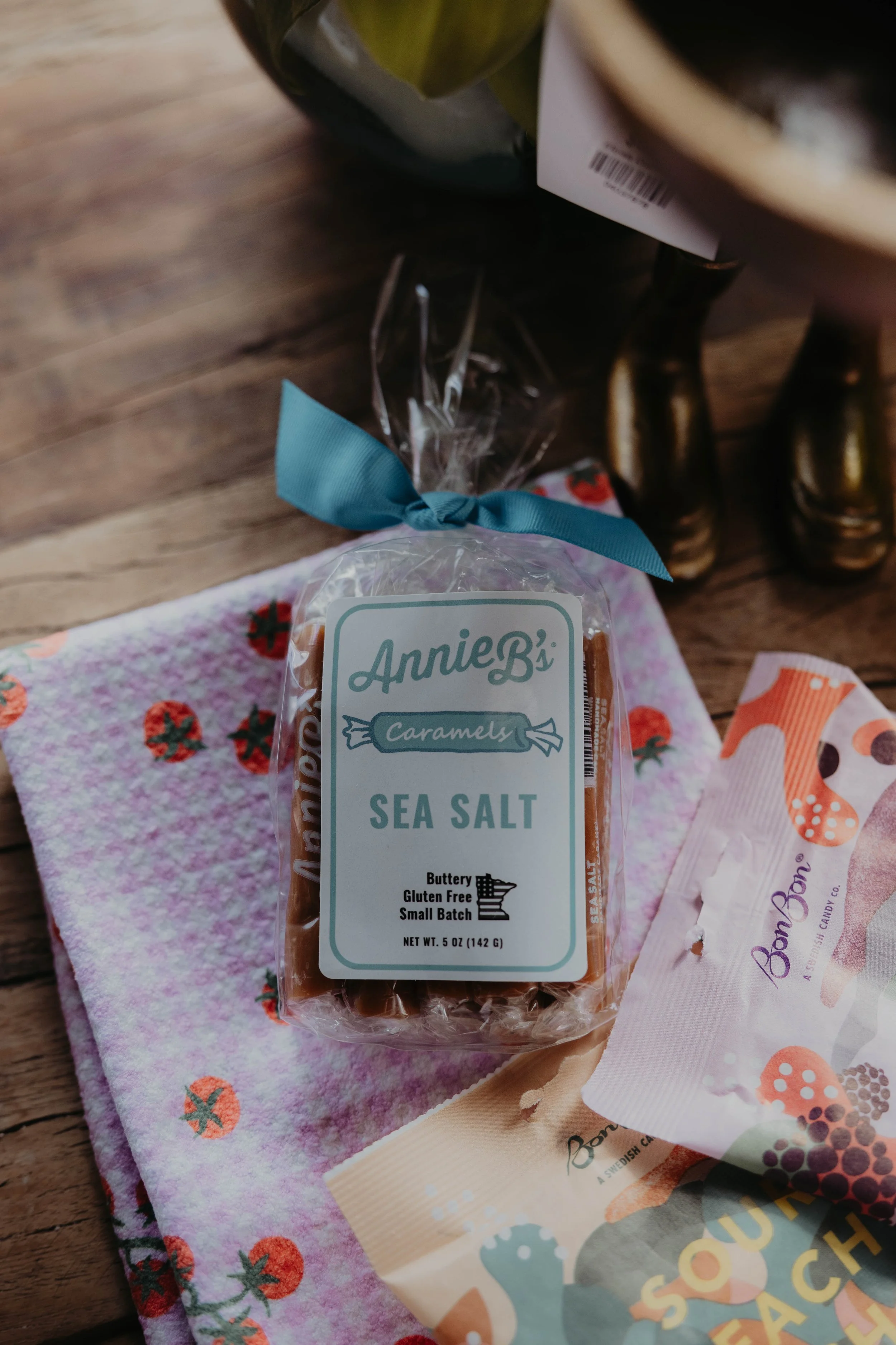 A package of Annie B's caramel sea salt candy on a floral towel with other candy packages nearby.