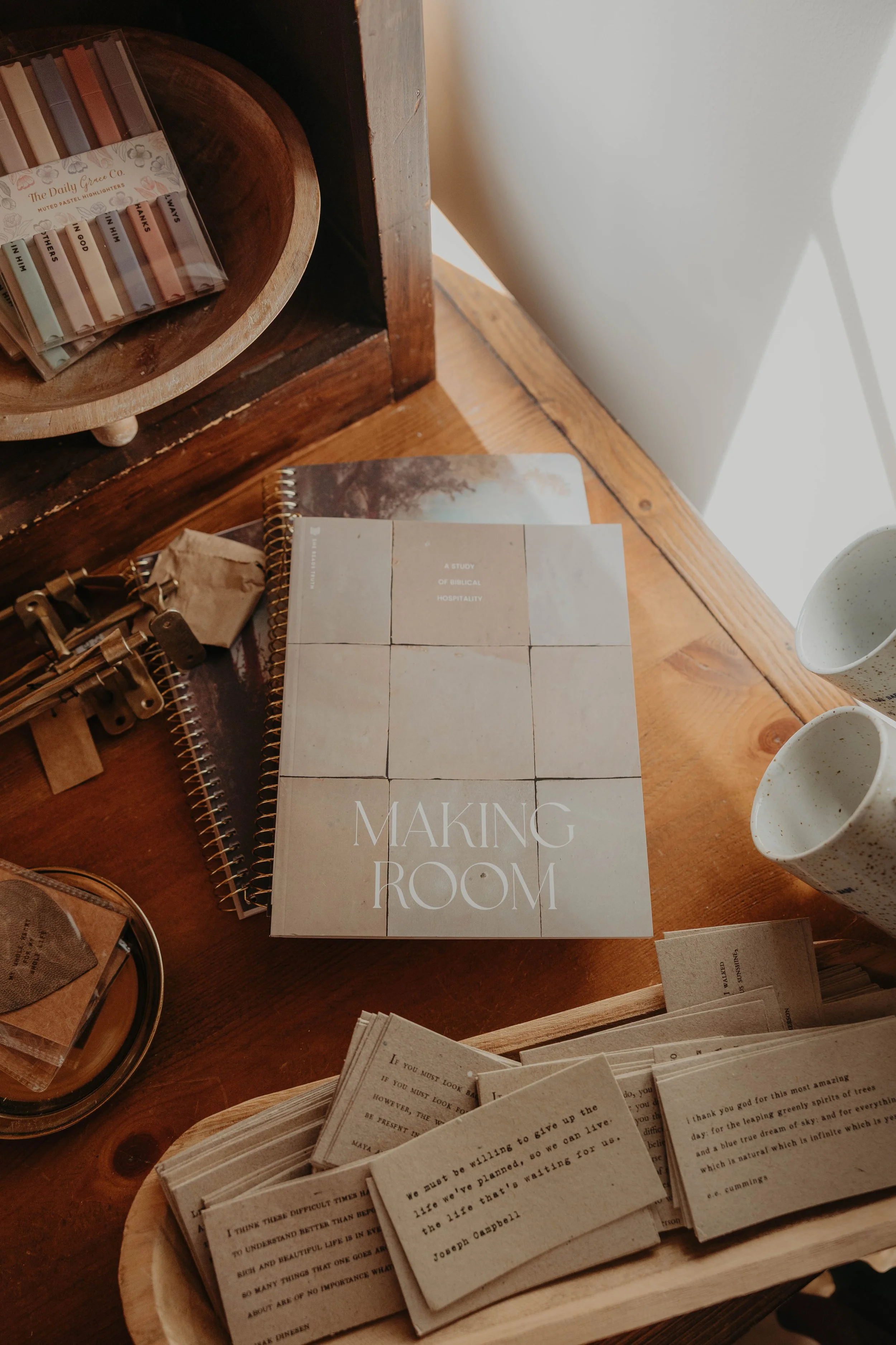 A wooden table with books and paper notes, a tray with pens, and a cup on the right side.