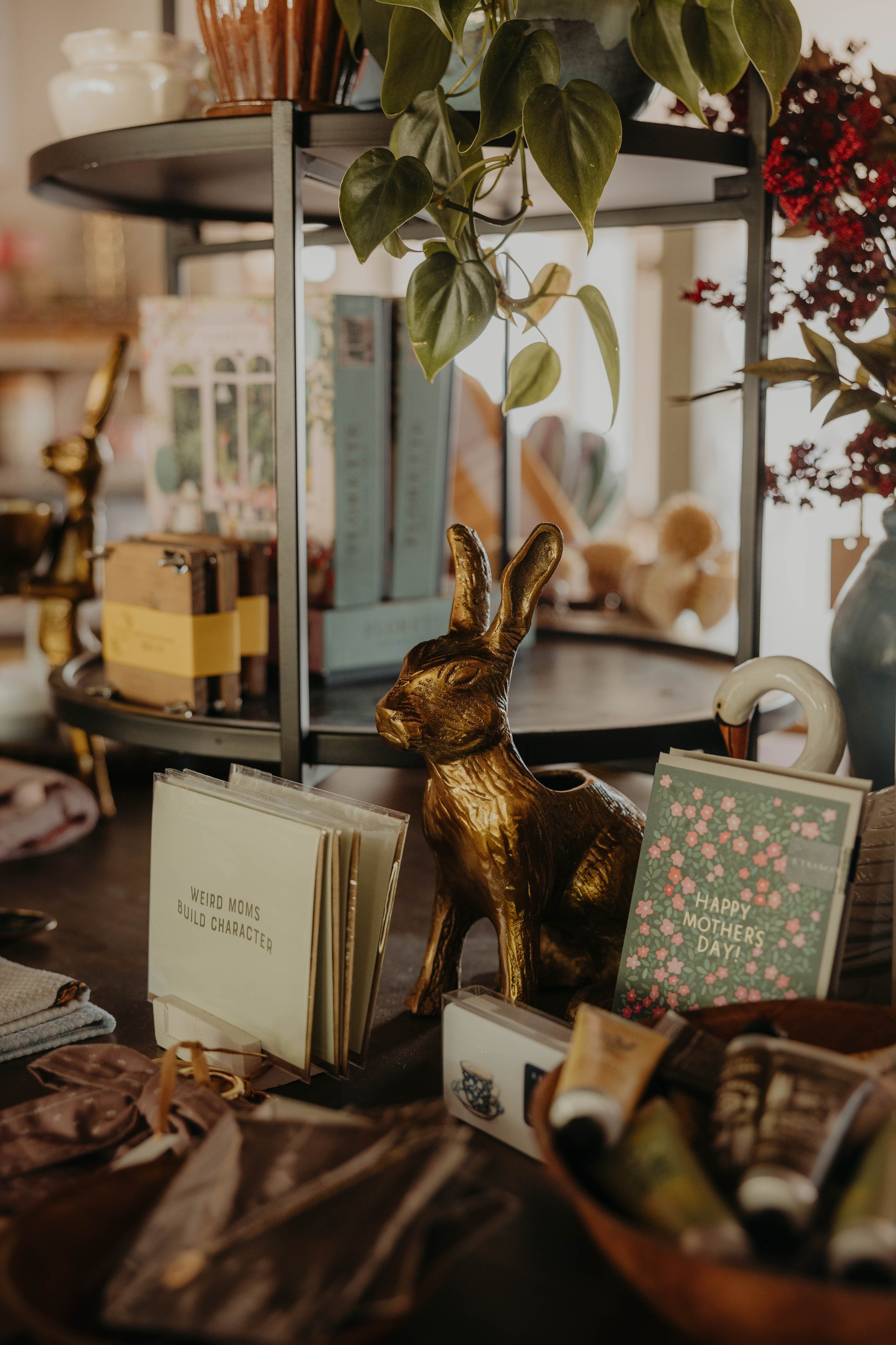 Decorative shelf with plants, books, greeting cards, and a gold rabbit figurine in a cozy store.