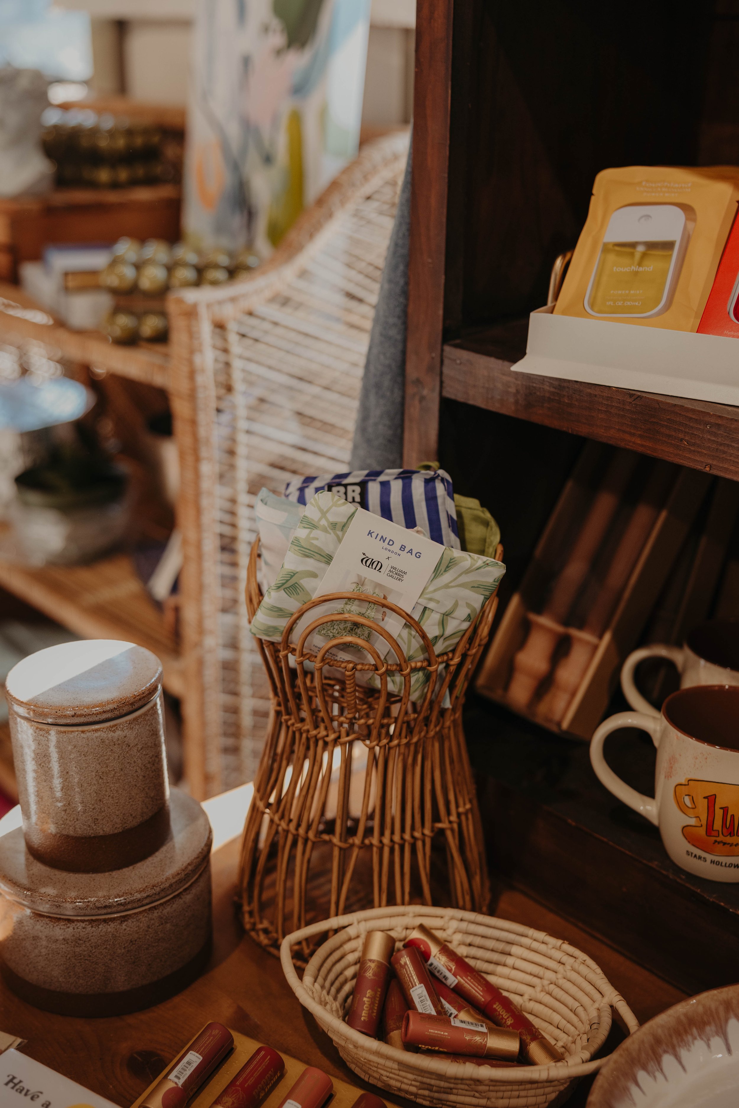 A display of various home decor items including candles, a wicker basket with lip balm, and mugs on shelves and a wooden table.