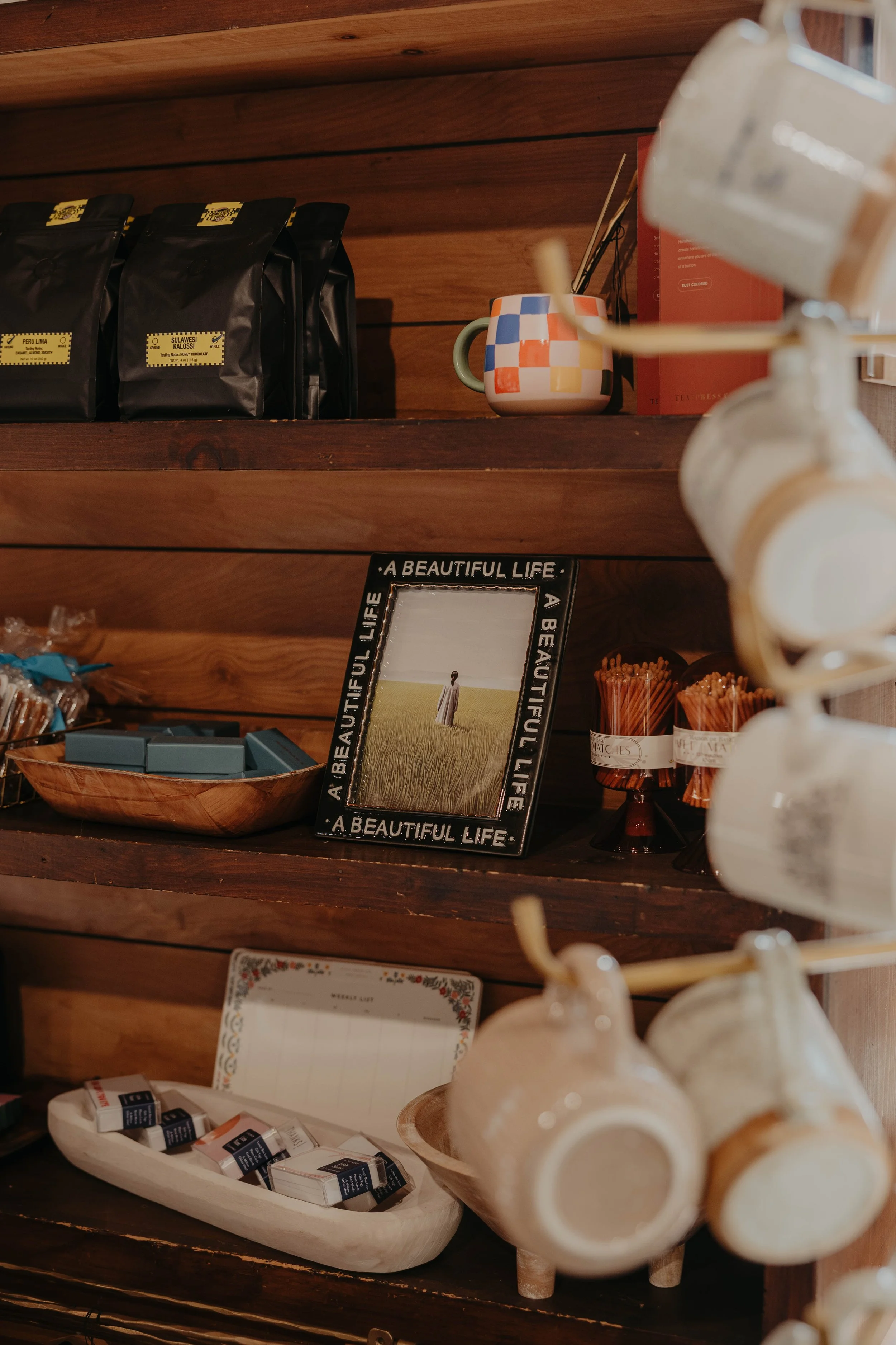 Wooden shelves displaying coffee bags, cups, a mirror with a quote, and various small items in a cozy shop interior.