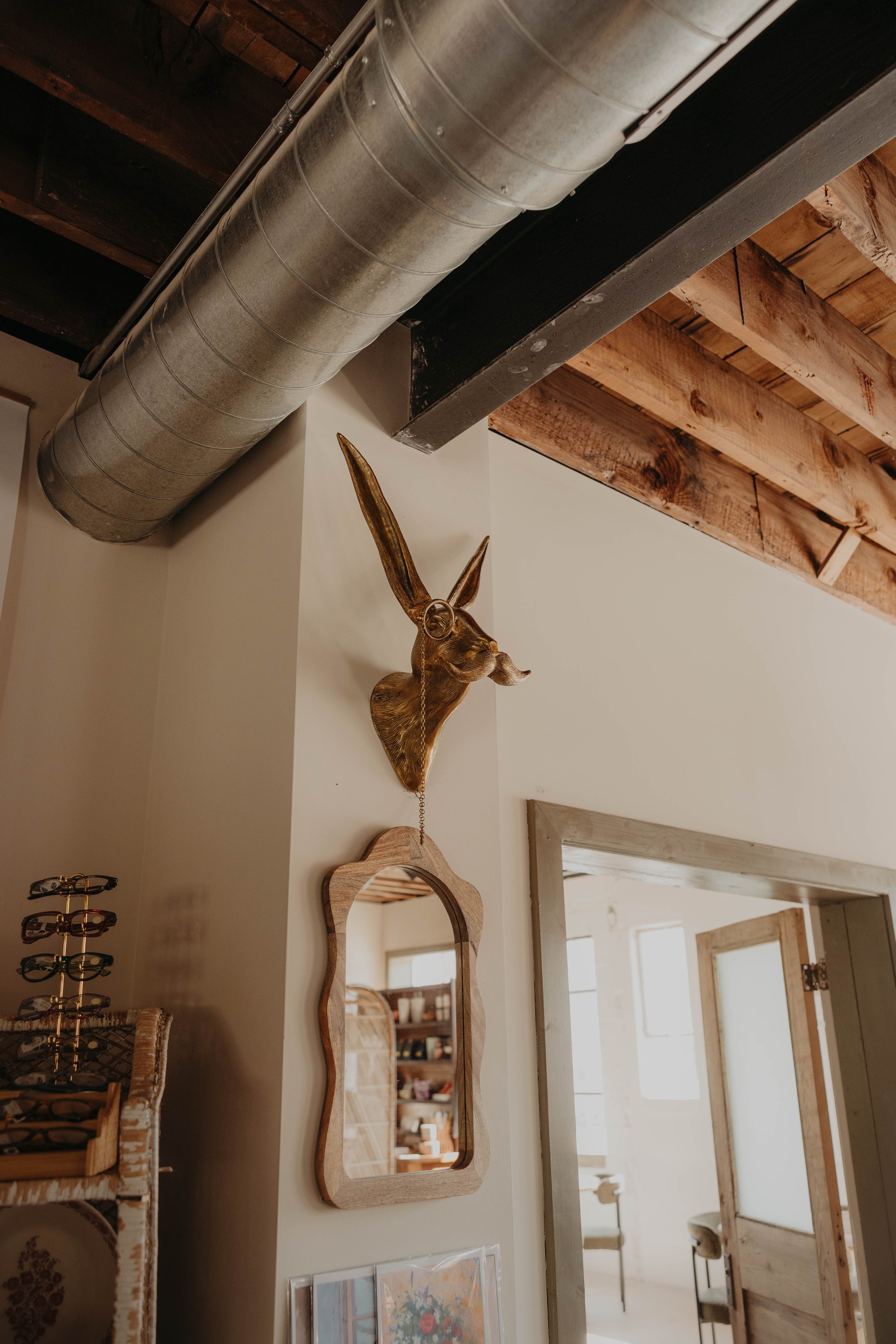 Interior view featuring a large metal industrial air duct, a wooden wall with exposed beams, a mounted deer head with antlers, and decorative mirrors on the wall.