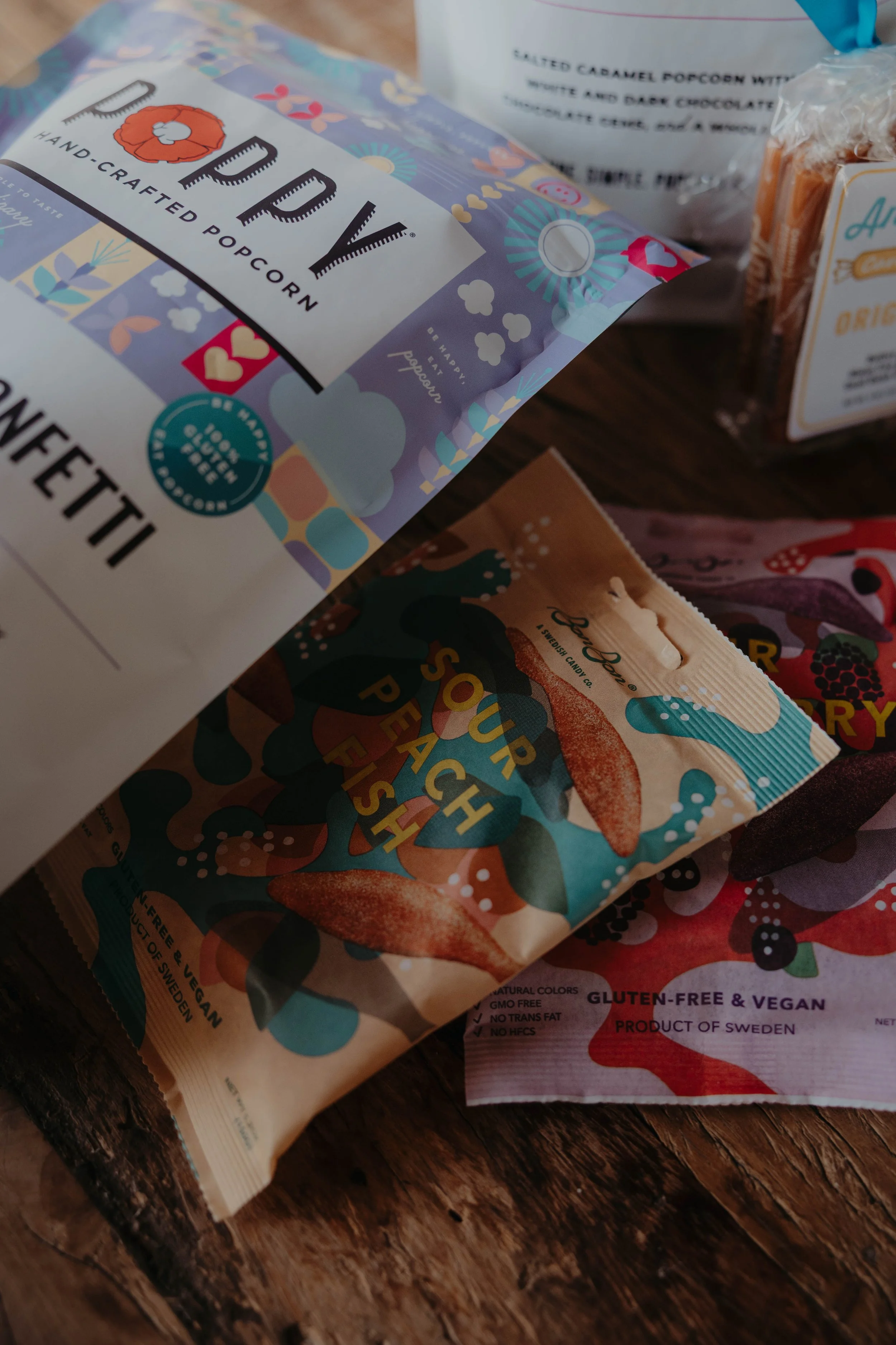 Close-up of colorful snack packages on a wooden surface, including a Health Warrior protein bita bar and other snack items in vibrant packaging.