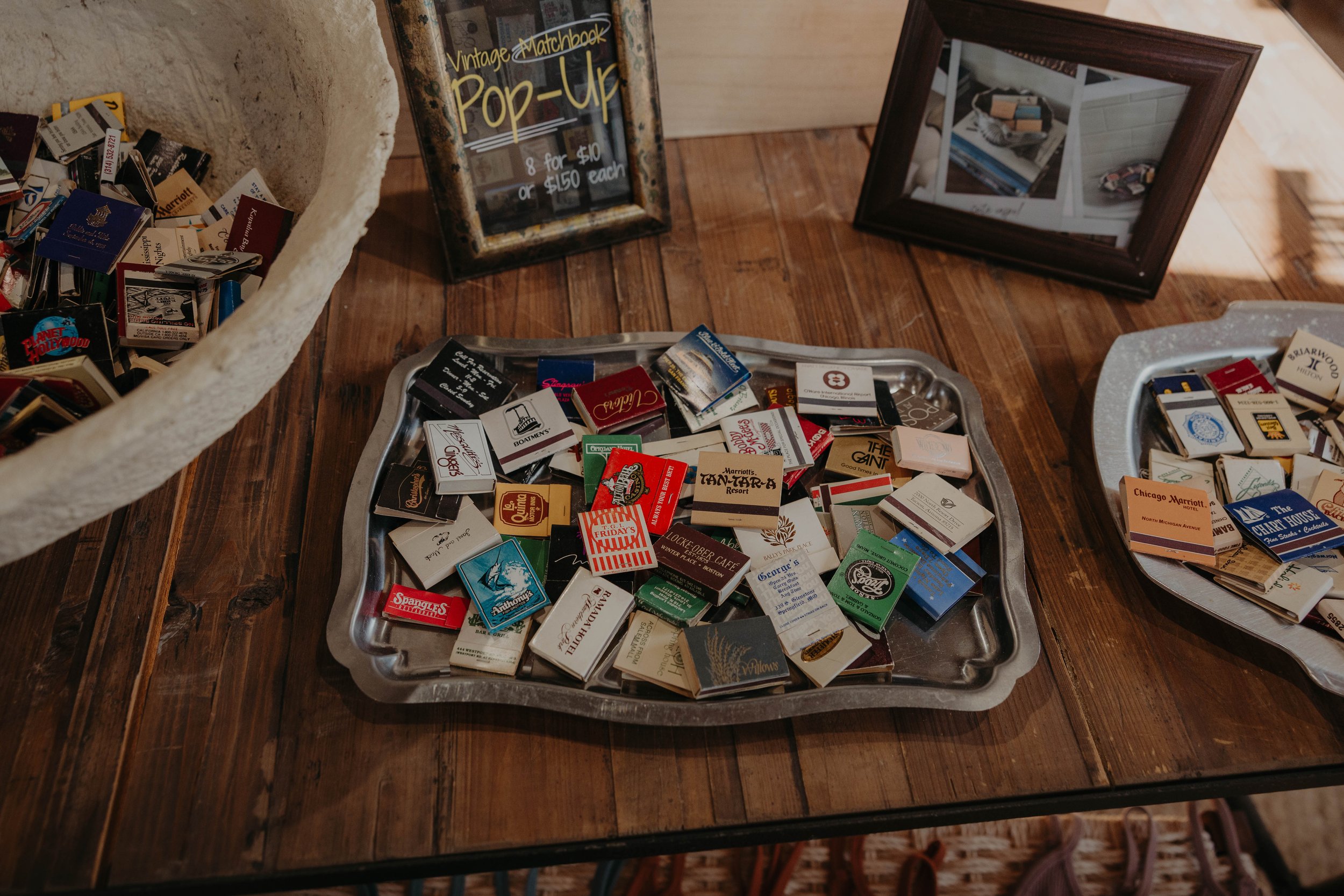 A table with trays of matchbooks, a framed mirror, and a sign advertising vintage matchbook pop-up sale.