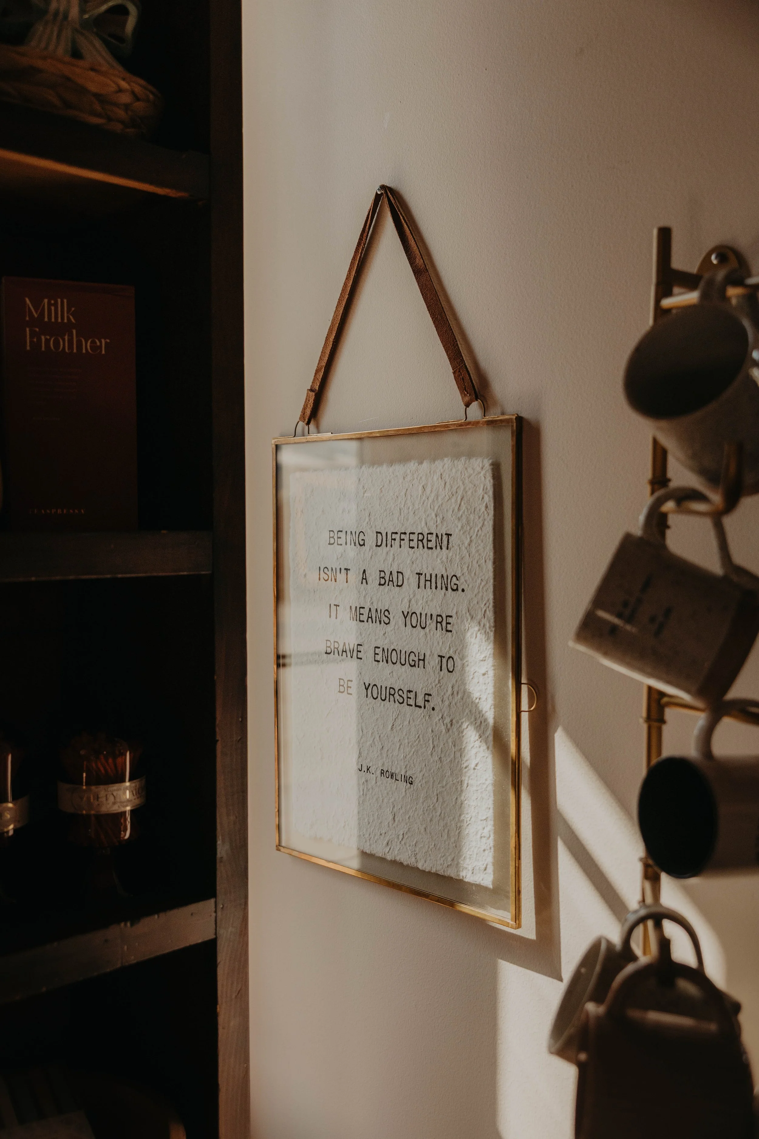 A framed quote on a wall with a cloth background, reading: "Being different isn't a bad thing. It means you're brave enough to be yourself."