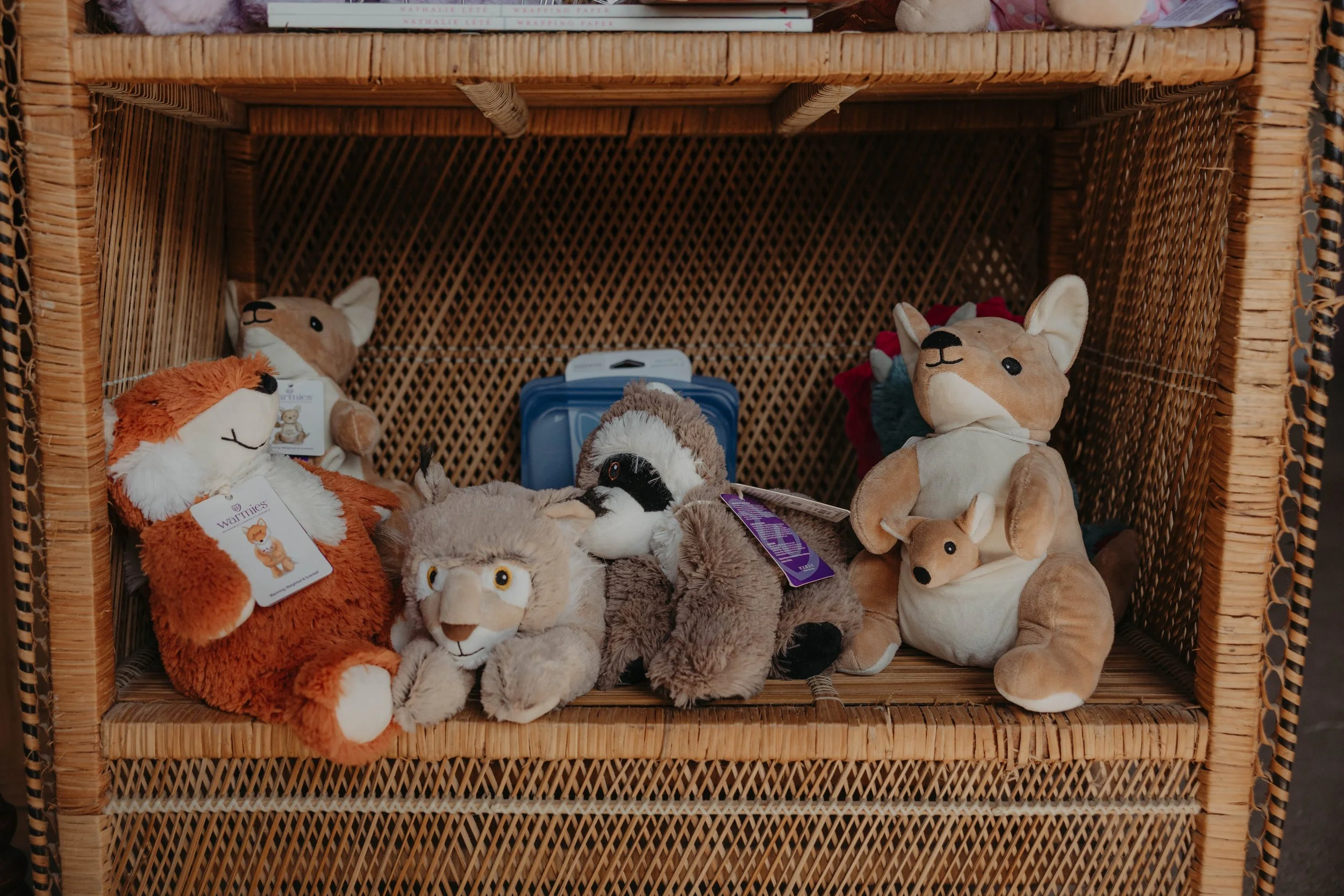 A wicker display shelf filled with various plush animal toys, including lions, foxes, raccoons, and other stuffed animals.