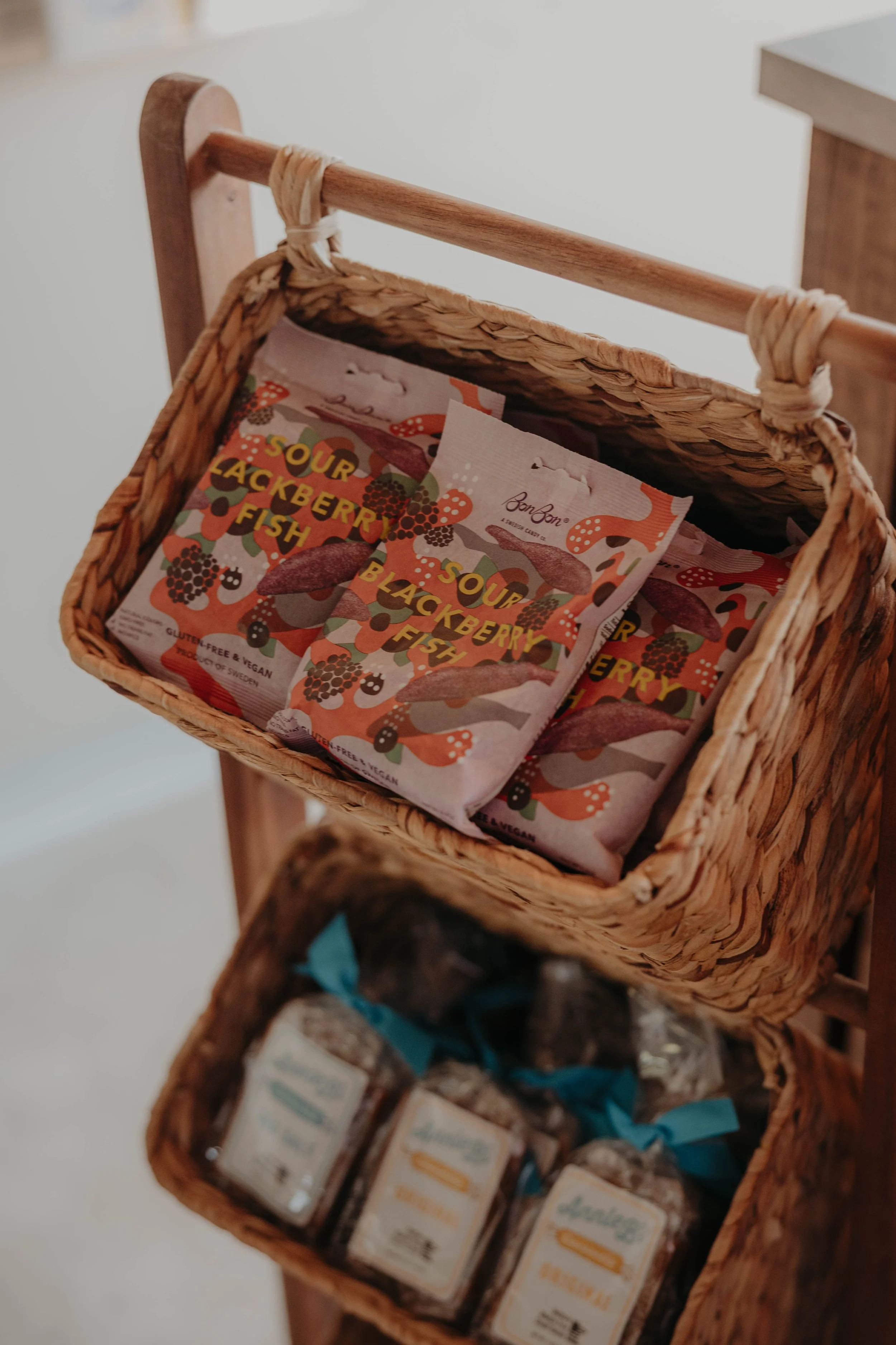 A wicker basket on a wooden stand containing packets of Sour Blackberry Fish and bottles of other snacks.