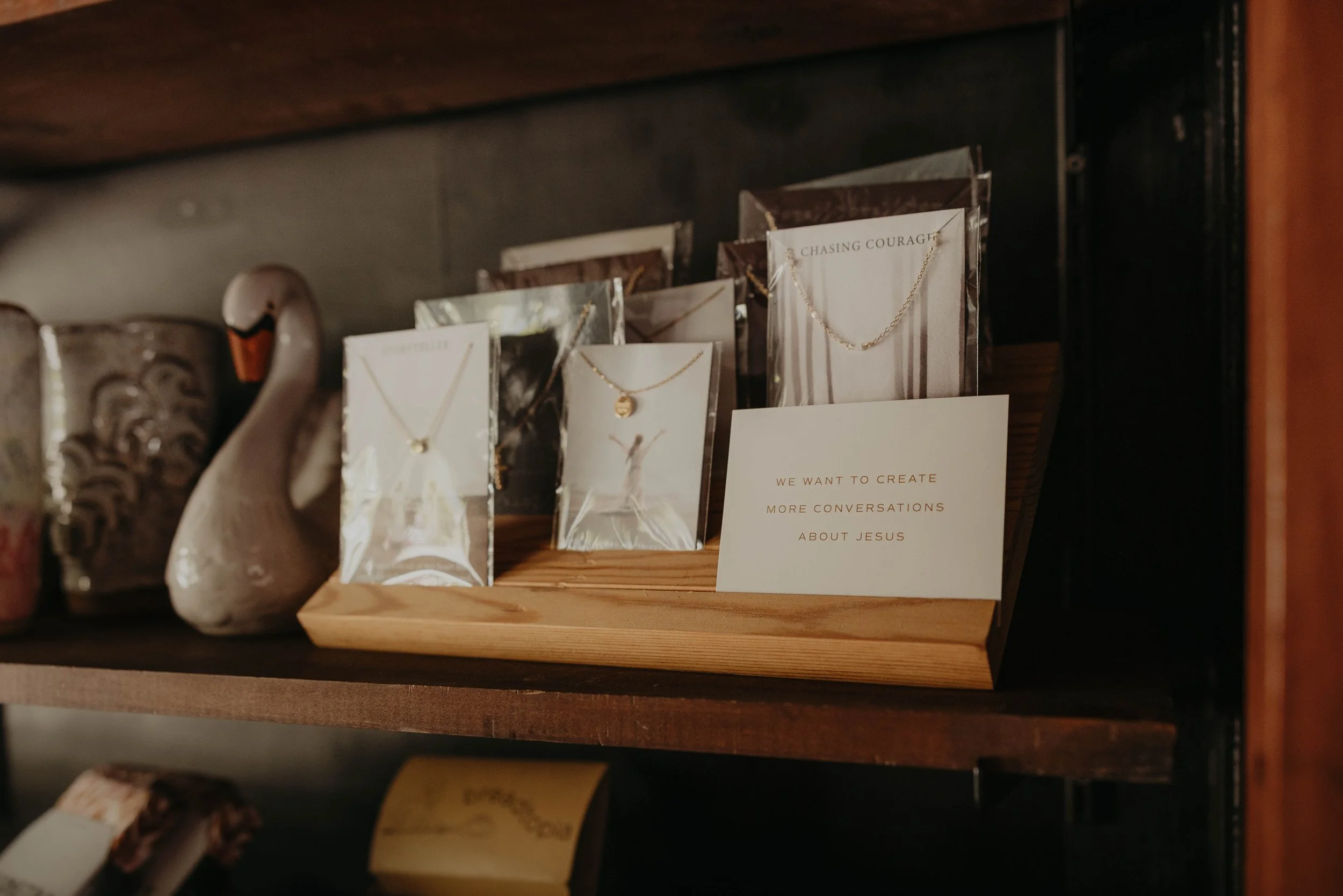 Display of jewelry including necklaces on cards, with a sign that reads: 'We want to create more conversations about Jesus'.