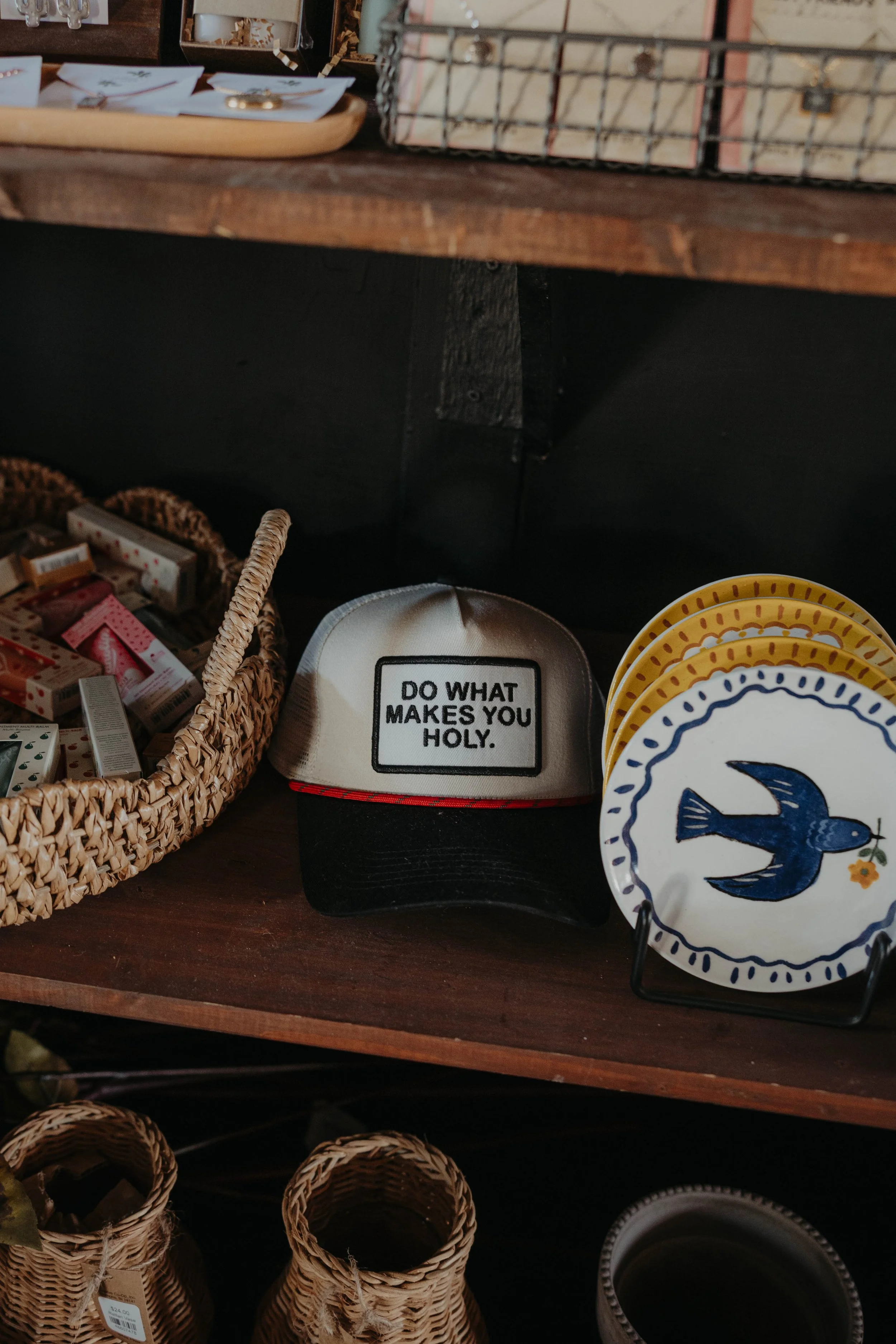 A display table with woven baskets, decorative plates featuring a blue anchor, and a container with a motivational quote. Background has storage bins and miscellaneous items.