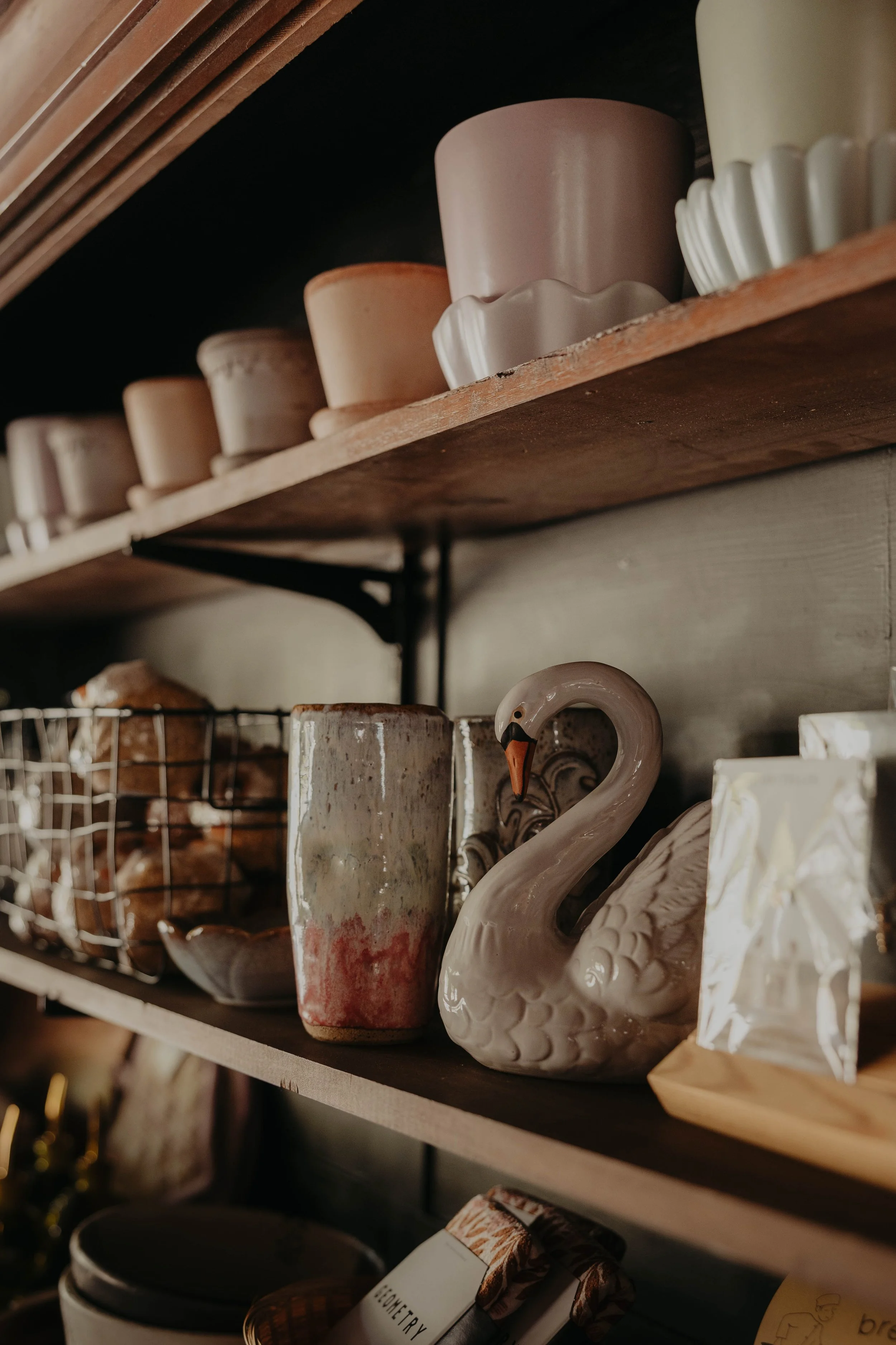 A wooden shelf displaying various ceramic items including cups, a swan-shaped teapot, and other decorative pieces in a store.