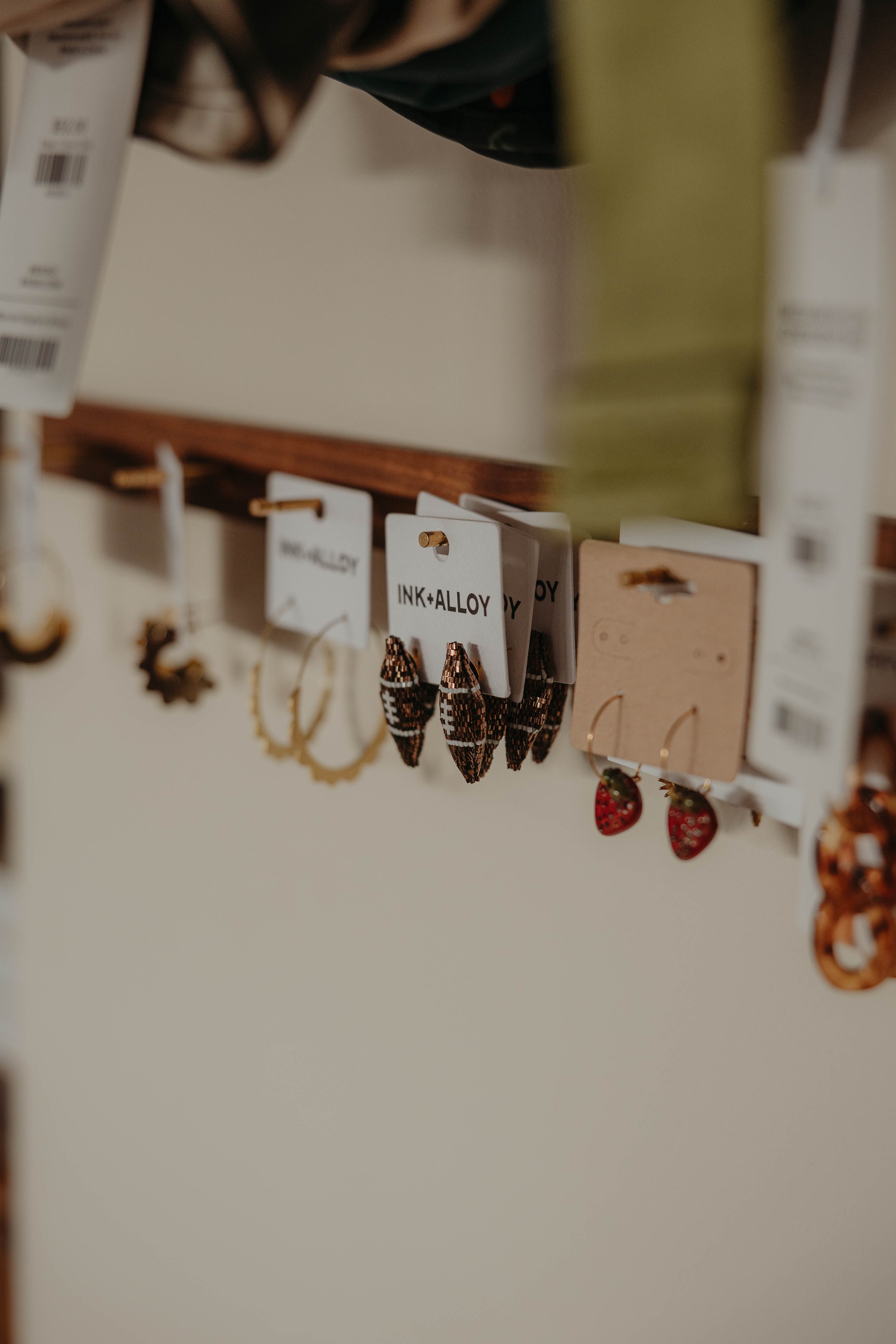 Close-up of earrings hanging on display hooks in a jewelry store, with tags labeled 'INK+ALLOY' visible in the image.