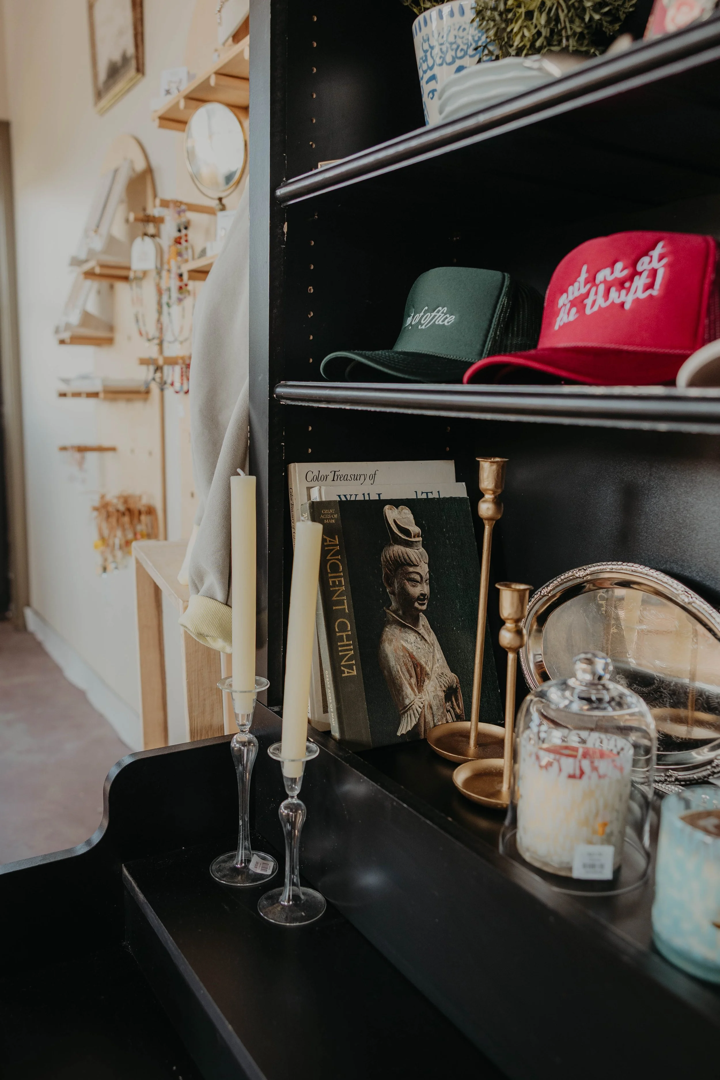 Display of decorative items including candles, books, a framed statue, and glass jars on a black shelf in a home decor store.