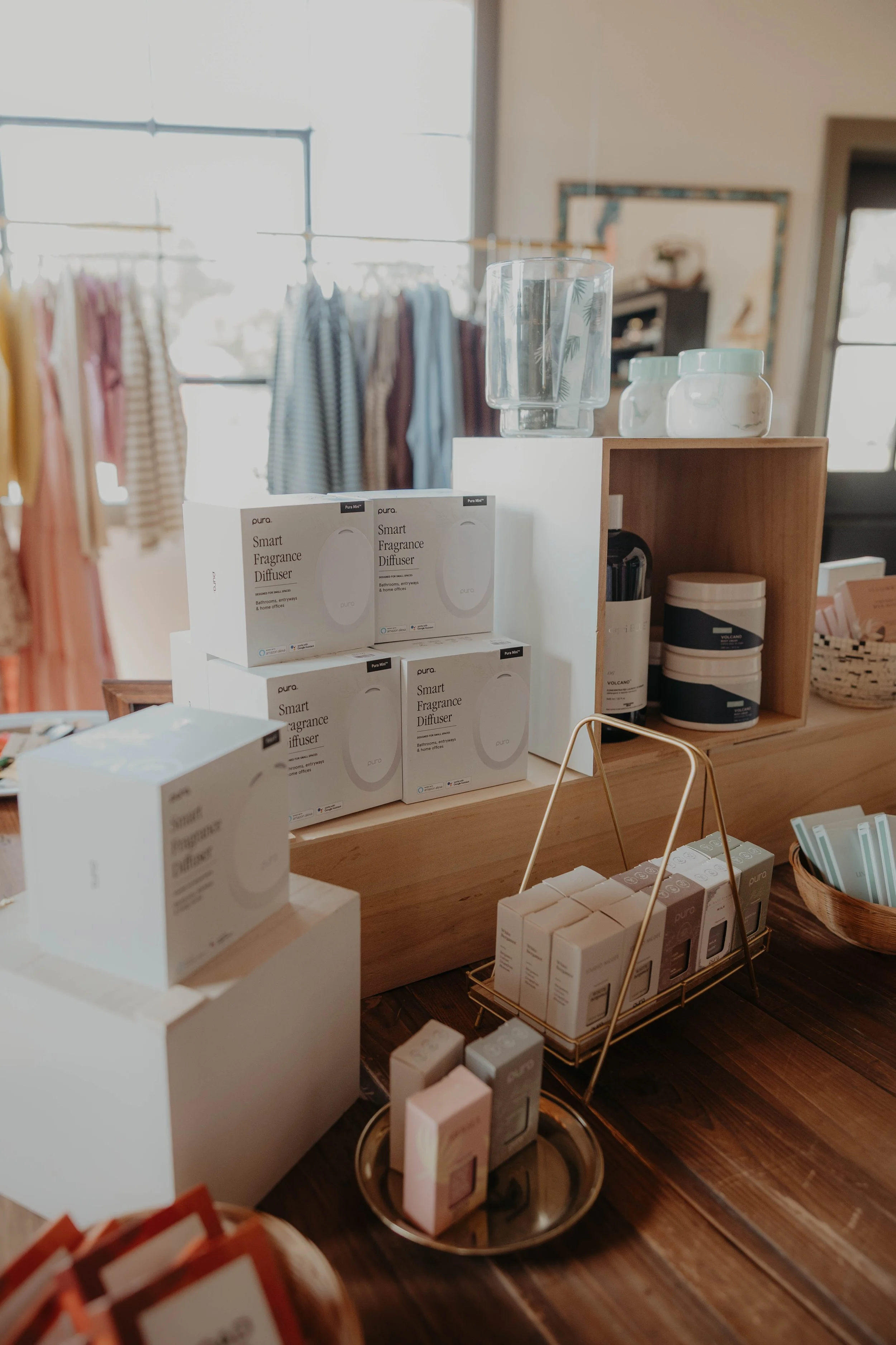 Display of scented products and fragrances in a store, with boxes labeled 'Smart Fragrance Diffuser' on a wooden surface and glass jars, with clothing items in the background.