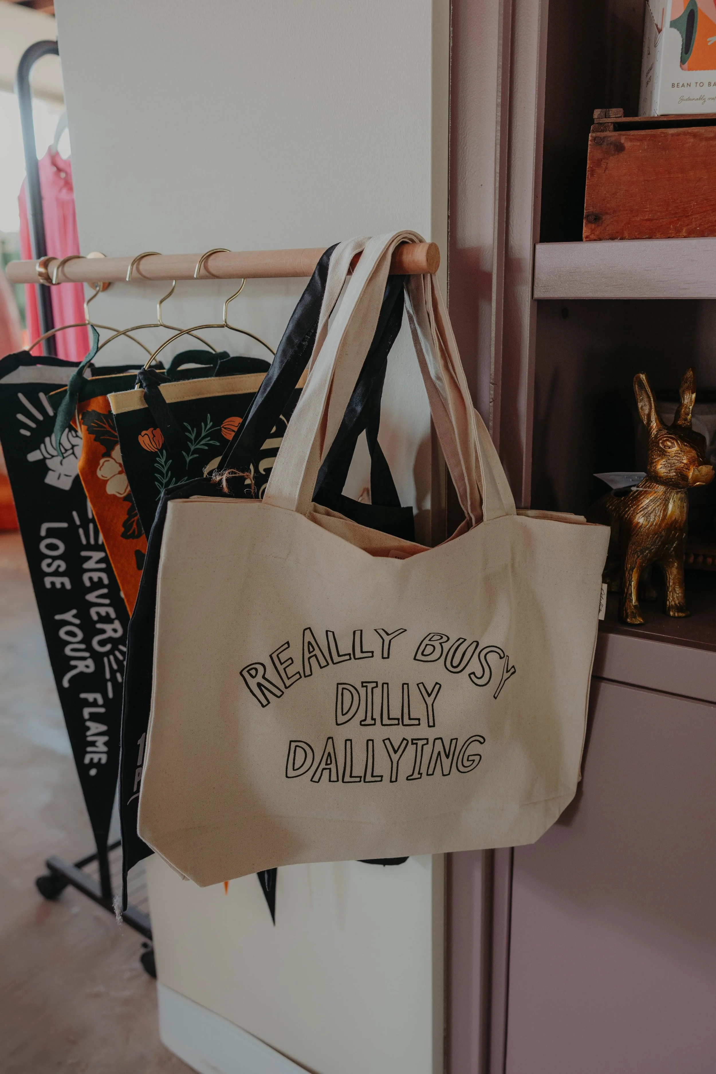 A beige tote bag with black text hanging on a wooden rack. The text says: 