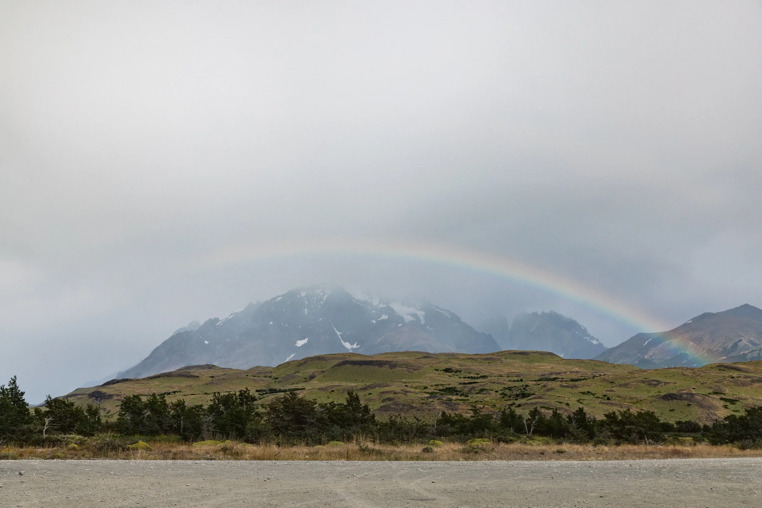 Mountain landscape with a rainbow above green hills and cloudy sky.