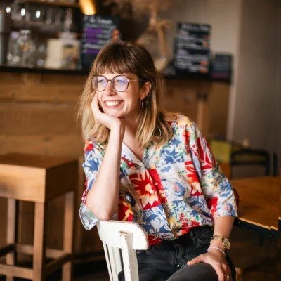 Une femme souriante avec des lunettes, assise dans un café
