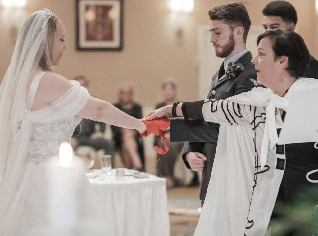 Bride and groom holding hands during wedding ceremony with officiant.