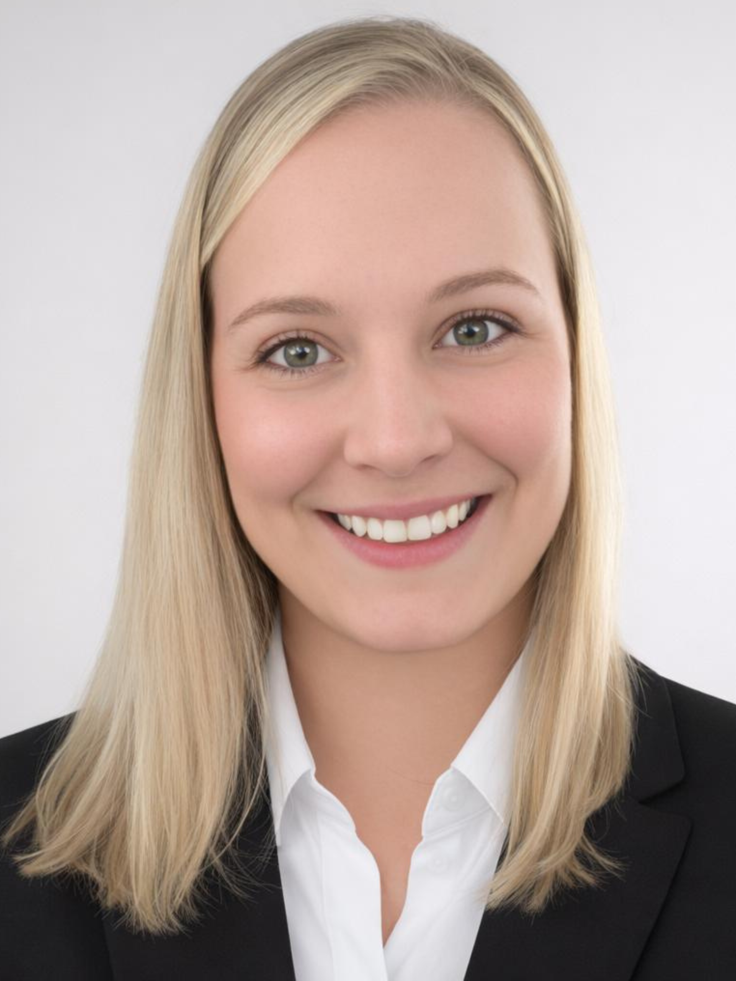 Headshot of a young woman with blonde hair, smiling, wearing a black blazer and white shirt.