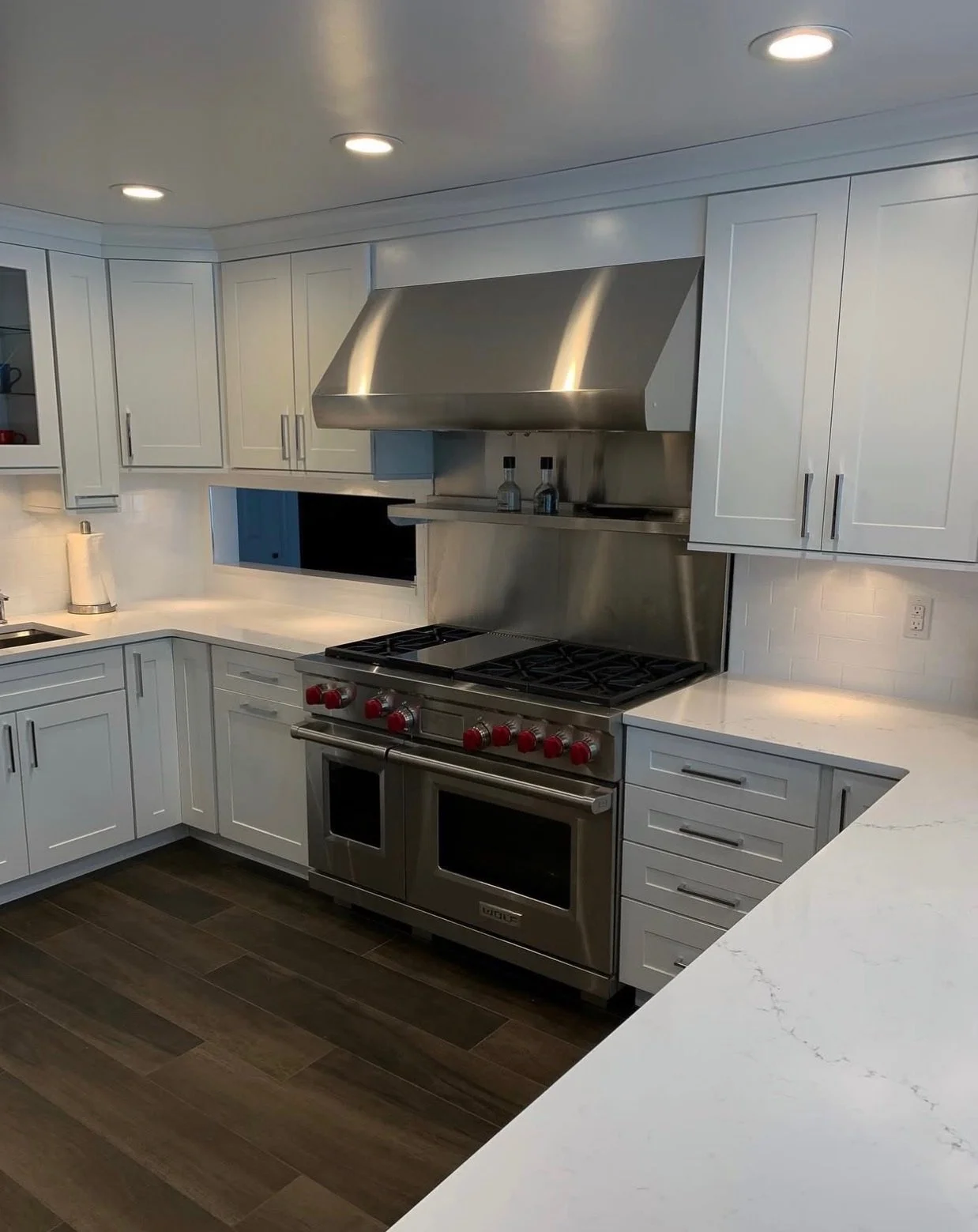 Modern kitchen with white cabinets, a stainless steel stove and oven, a stainless steel range hood, and dark wood flooring.