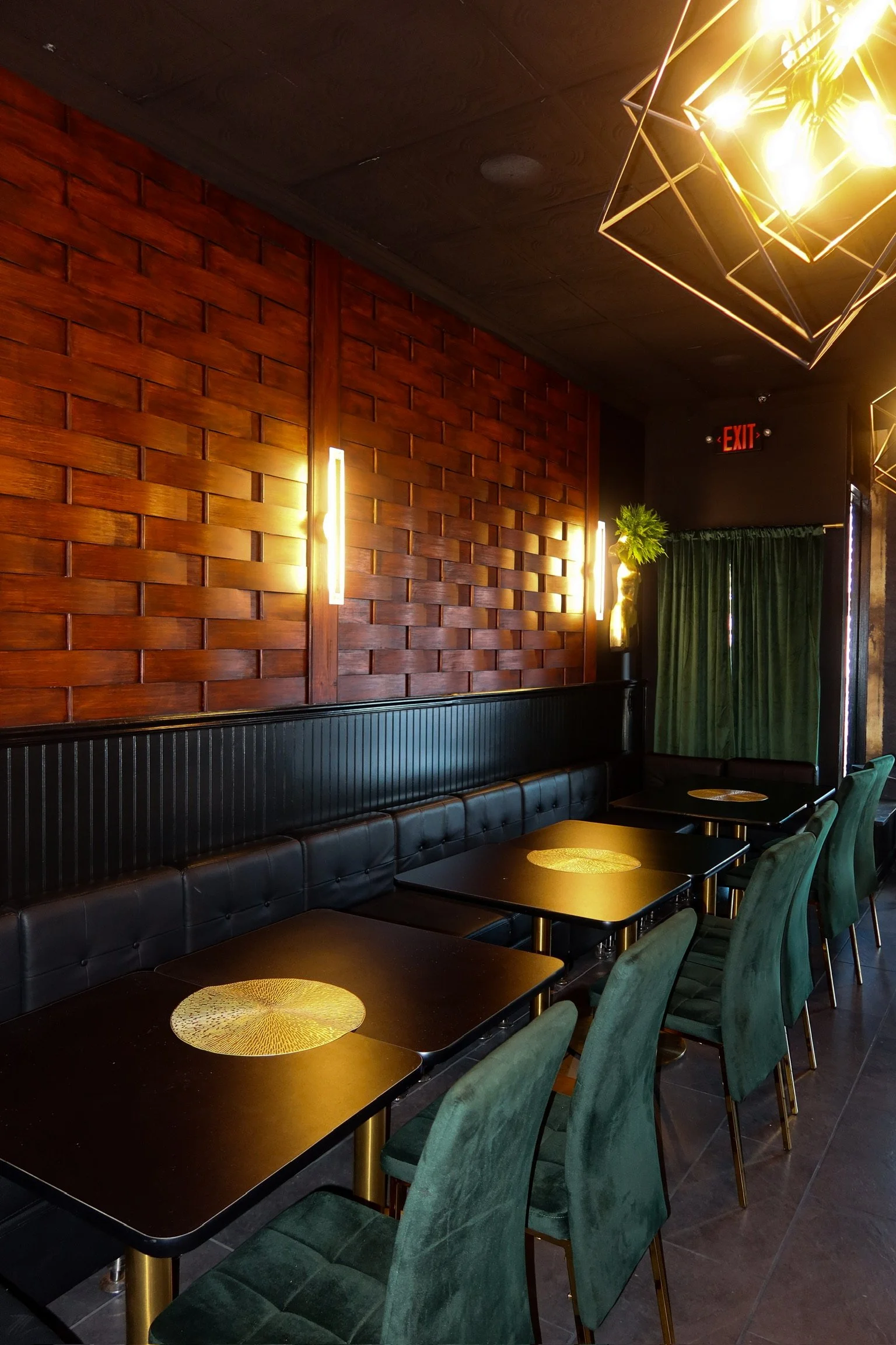 Interior of a restaurant or bar with black tables, green chairs, a black cushioned bench, wooden accent wall, and modern lighting fixtures.