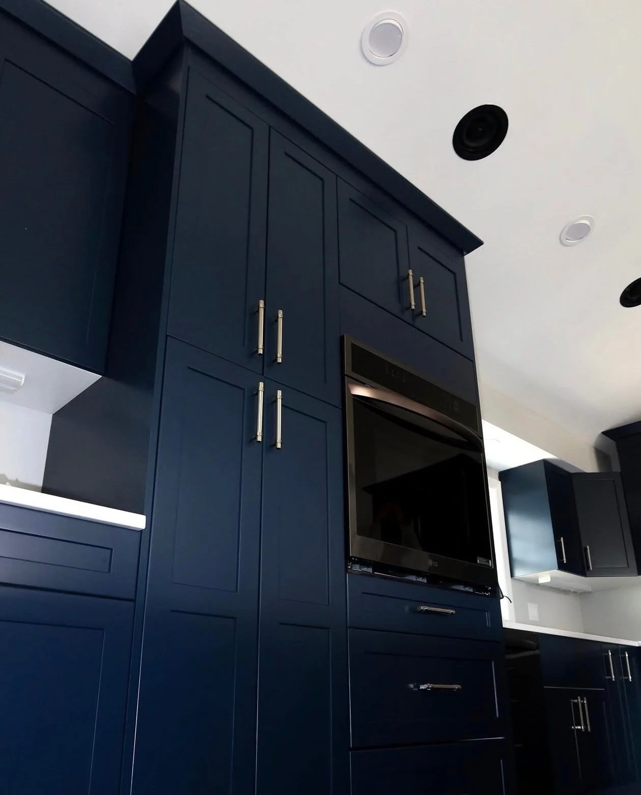 Kitchen with navy blue cabinets and built-in black oven, ceiling with recessed lighting.