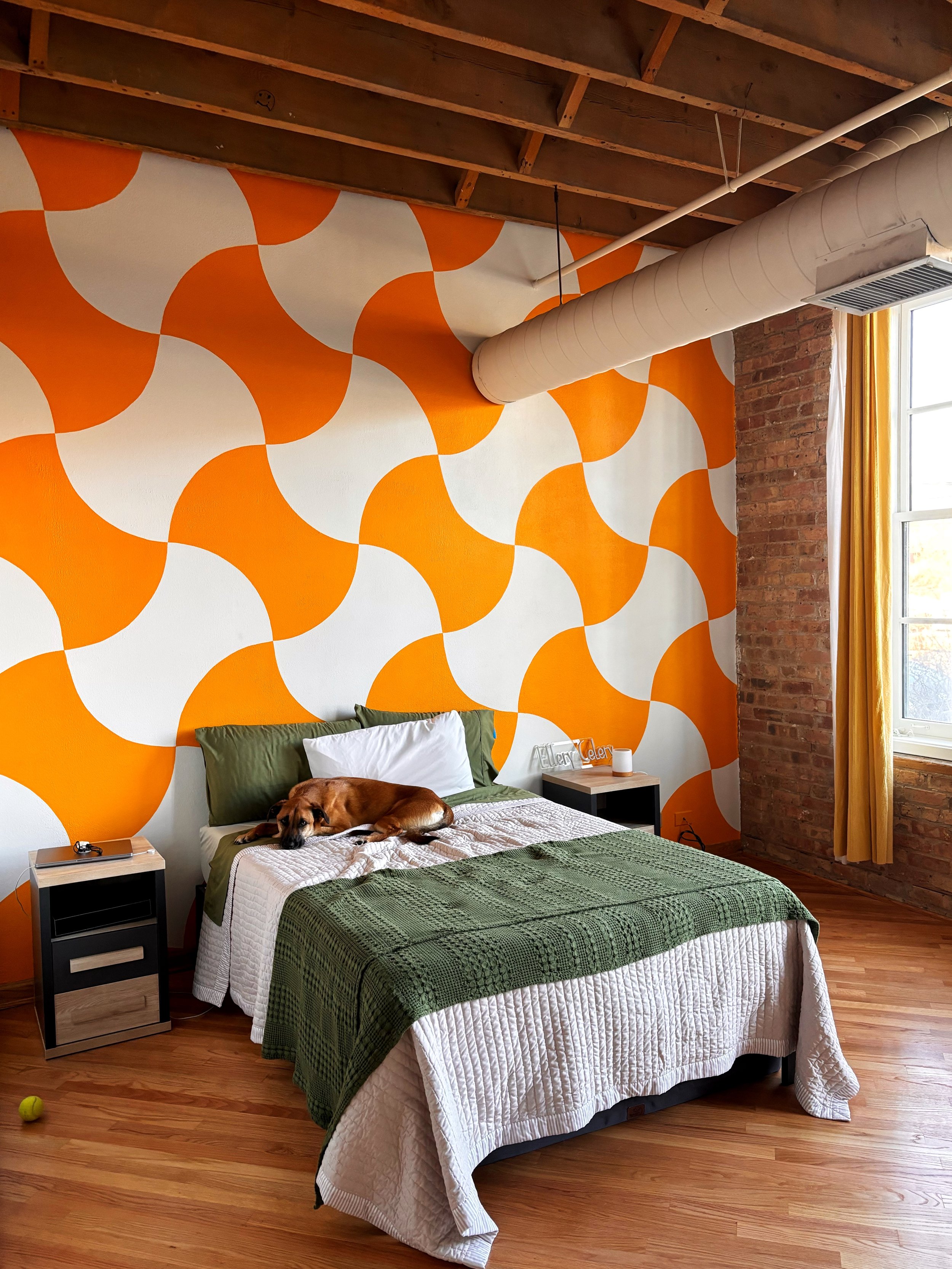 A bedroom with a large orange and white geometric patterned accent wall. Residential mural.