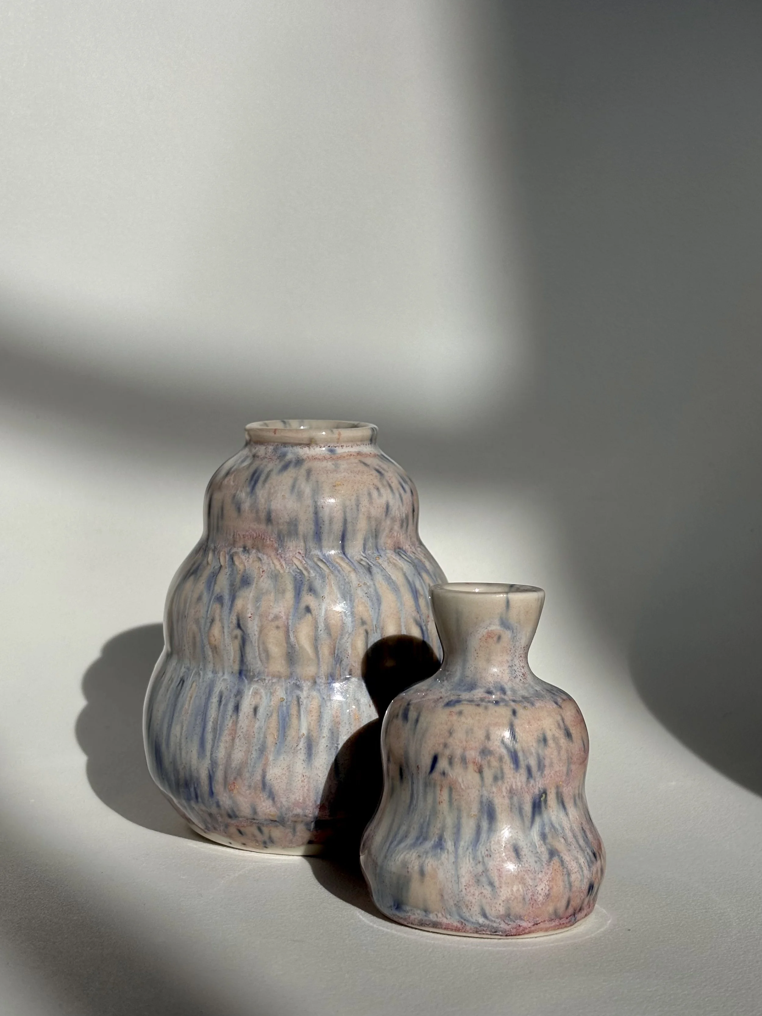 Two ceramic vases with marbled blue, beige, and pink patterns on a white surface, casting shadows under natural light.