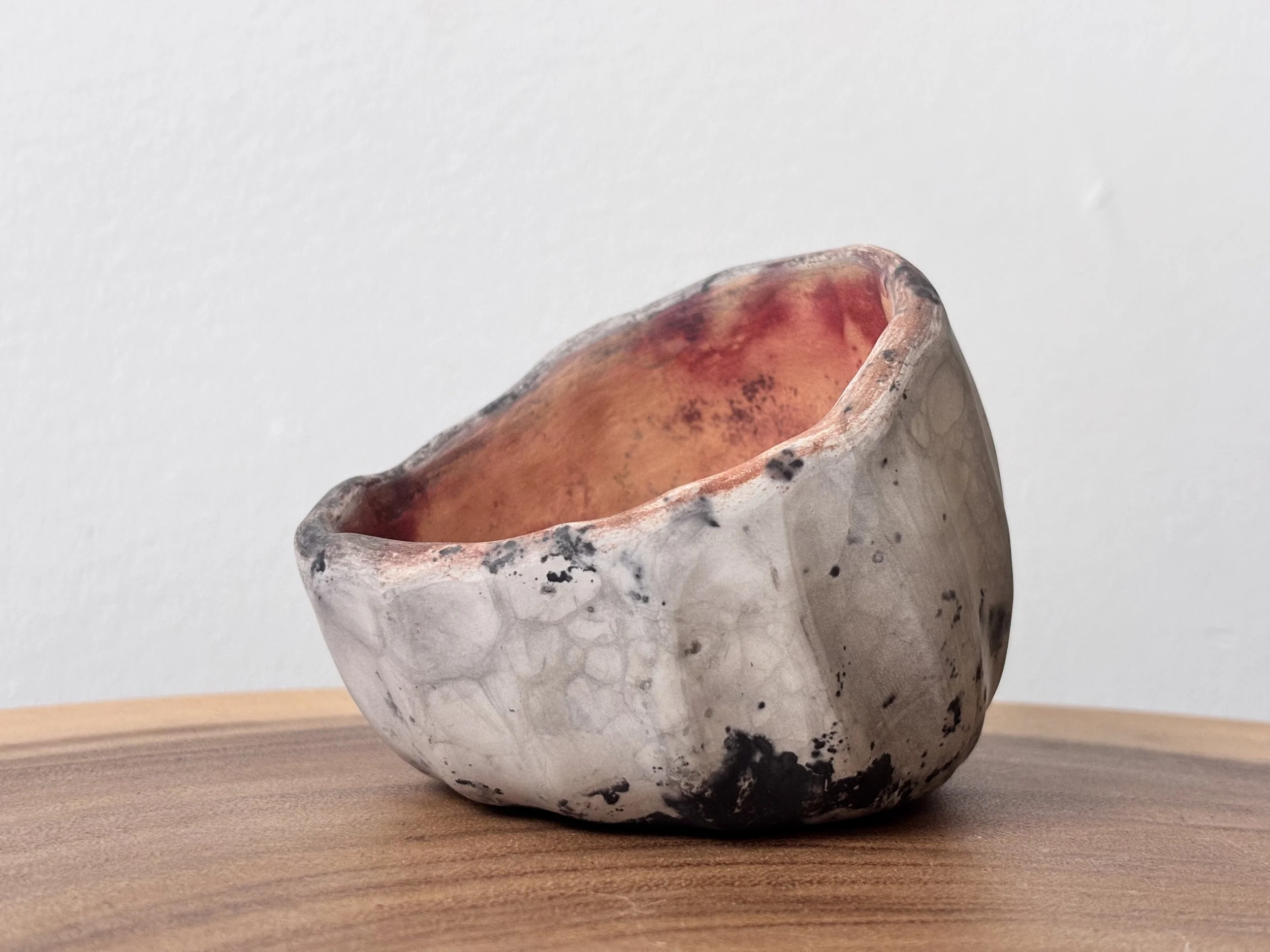 Ceramic bowl with a textured, natural finish, placed on a wooden surface against a plain white wall.